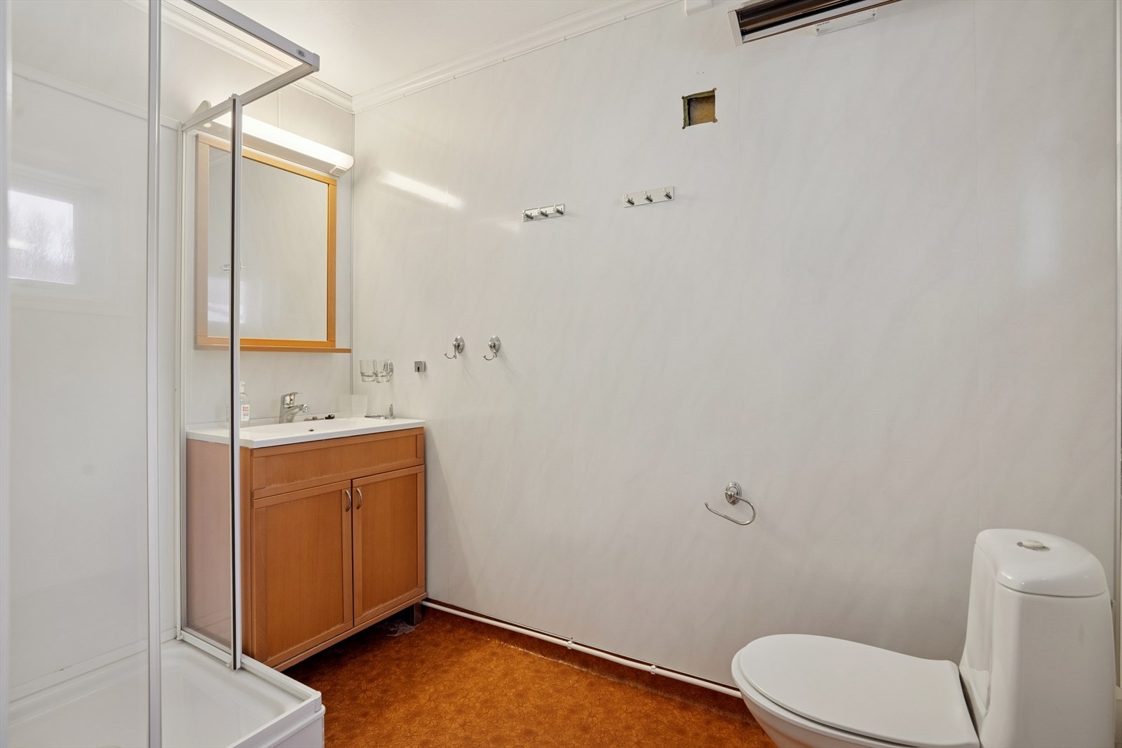 Badet består av speil, servant med seksjon, gulvmontert toalett og dusjkabinett. Galleribilde