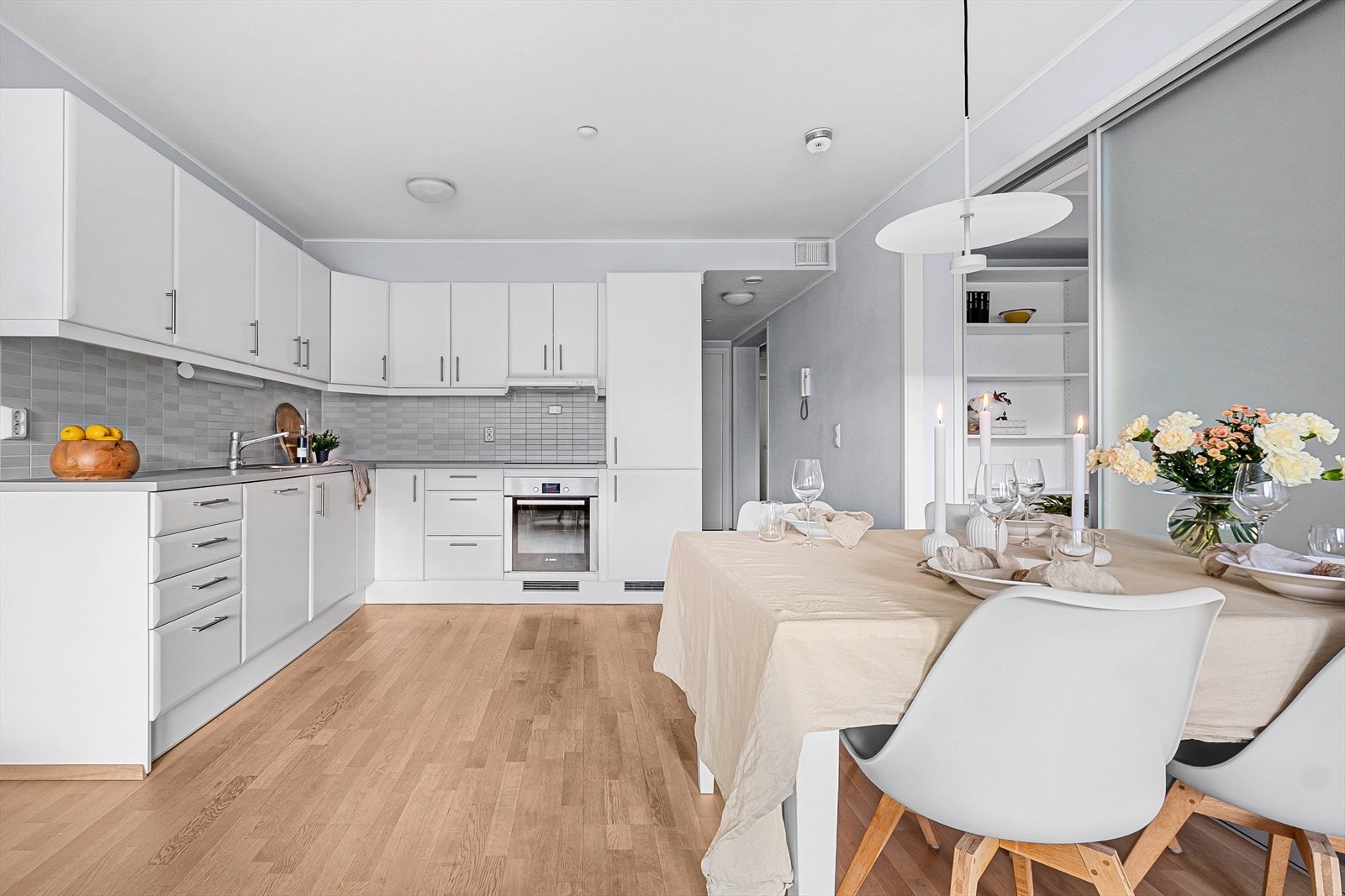 Kjøkkenet har en tidløs innredning med hvite glatte fronter, benkeplate i laminat med nedfelt kjøkkenvask og fliser på vegg over benk Galleribilde