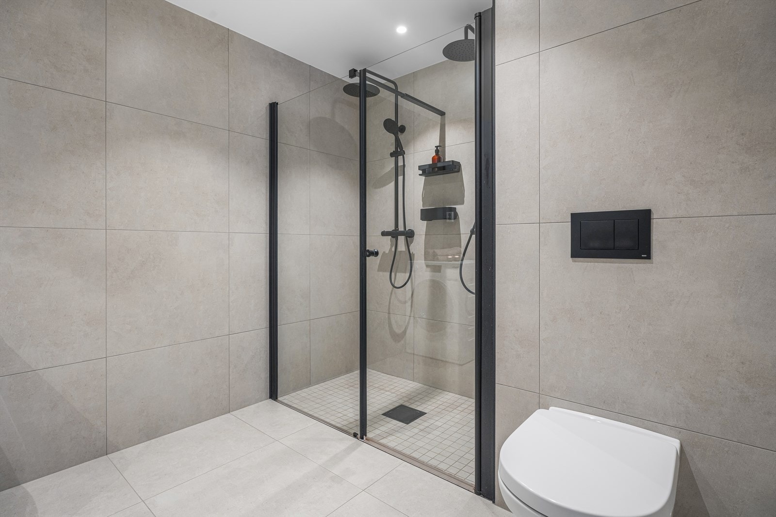 Videre er det en nedsenket dusjsone med to dusjer og skjermvegger i glass, samt opplegg for vaskemaskin. Galleribilde