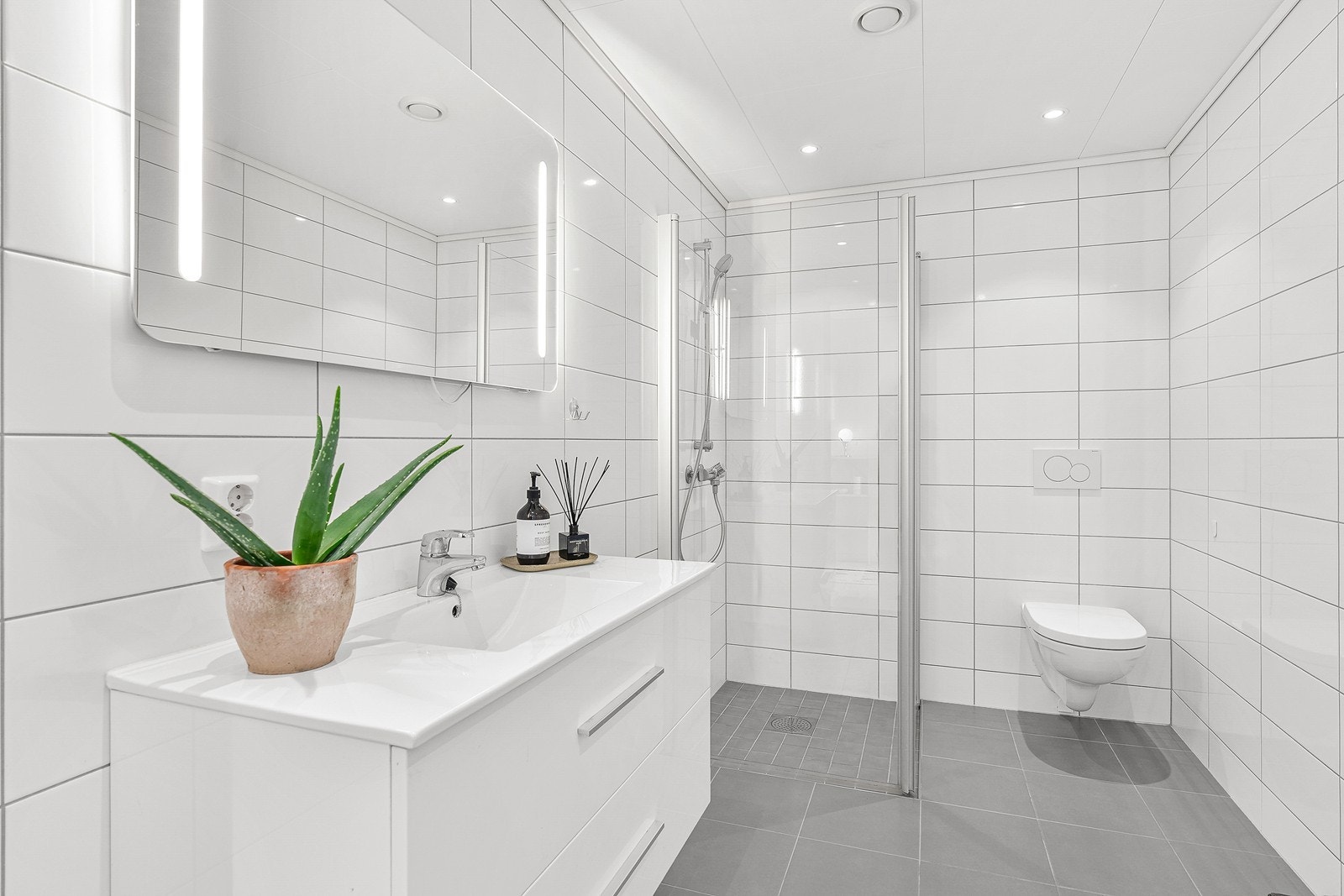 Badet er helfliset og innredet med servant med underskap, speil med lys, dusjhjørne og vegghengt WC. Galleribilde