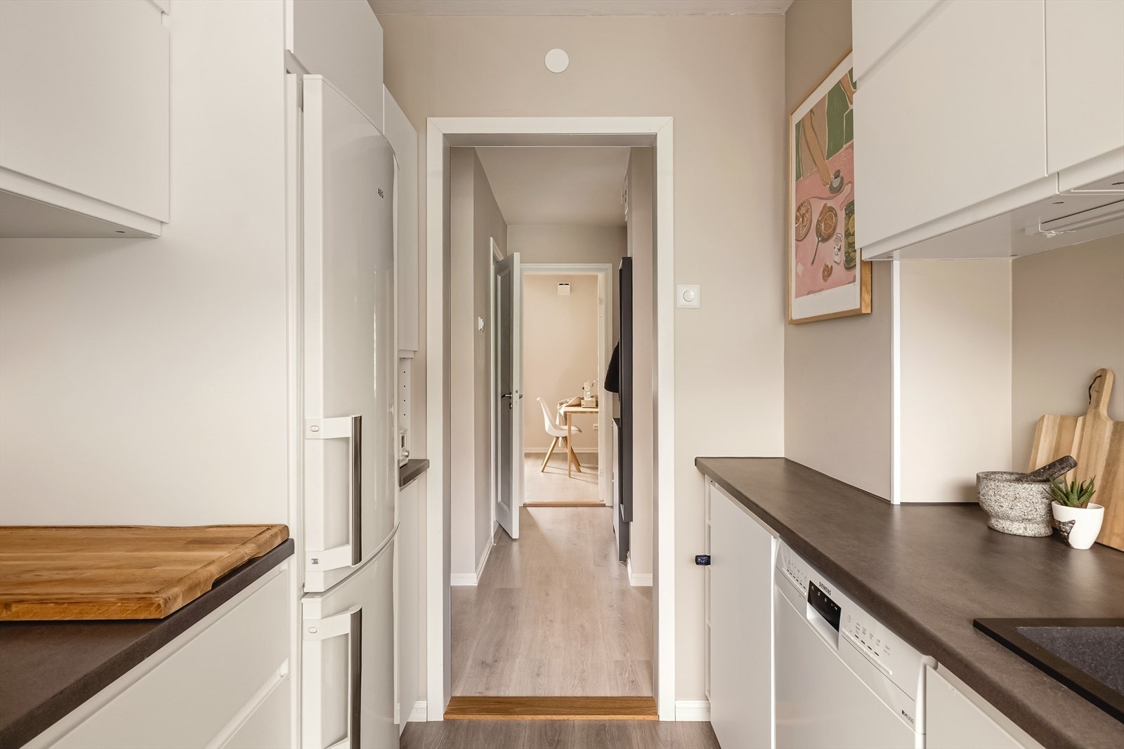 Innredning med slette fronter i hvit utførelse, lys under overskap, laminert benkeplate og veggflater malt i en lun, behagelig fargetone. Galleribilde