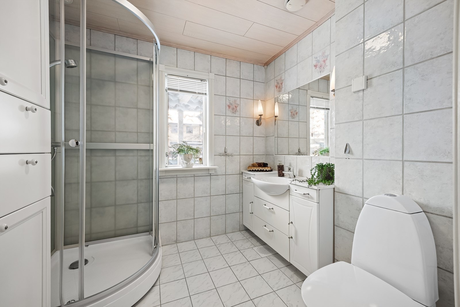 Flislagt bad med varmekabler i gulv. Badet er innredet med baderomsinnredning med glatte fronter, speil over servant, toalett, servant og dusjkabinett. Galleribilde