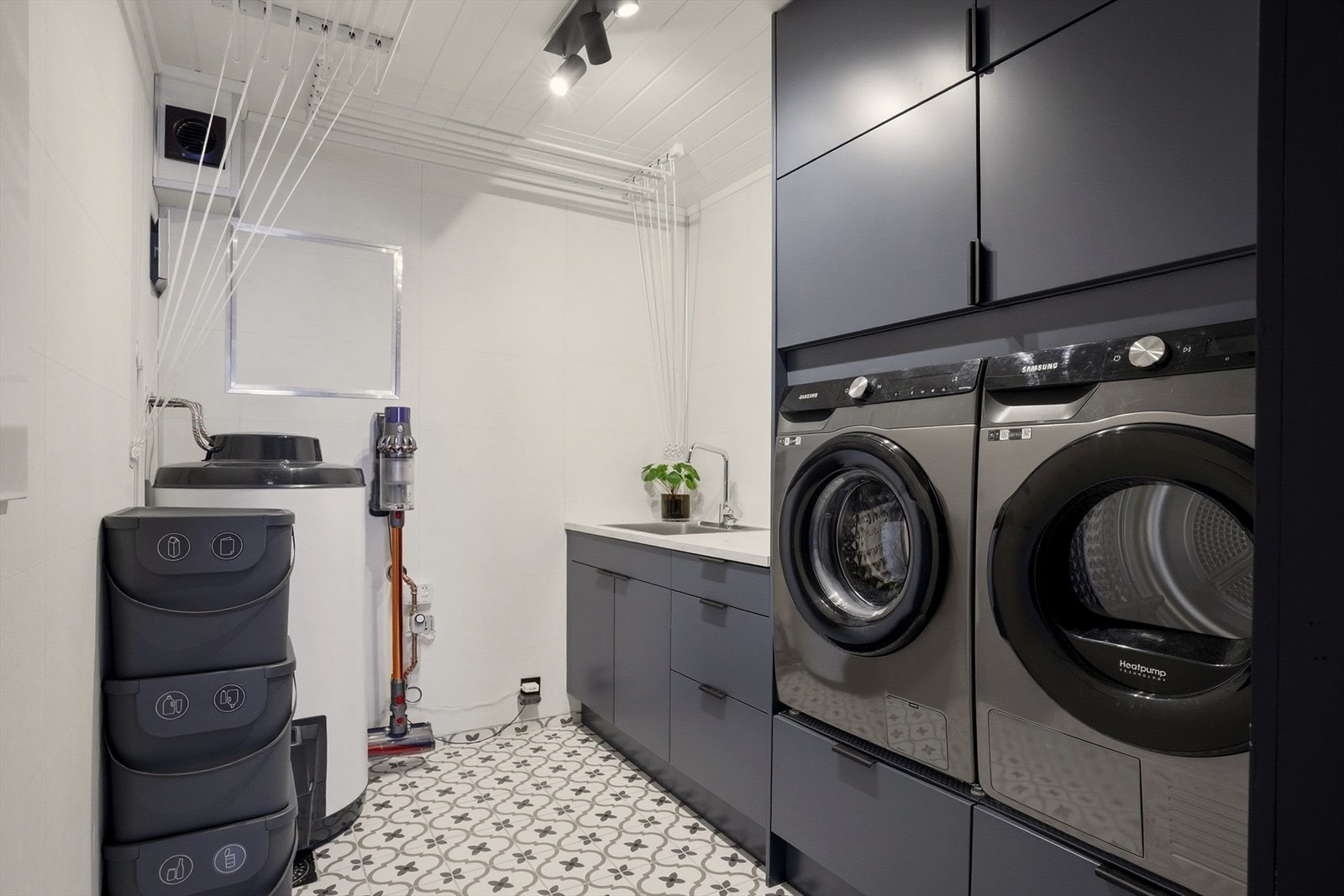 Dette vaskerommet er praktisk, moderne og svært godt utnyttet. Her får du gode oppbevaringsmuligheter med gjennomgående skapløsninger, en romslig benkeplate med vask, samt både vaskemaskin og tørketrommel plassert i ergonomisk høyde. Galleribilde