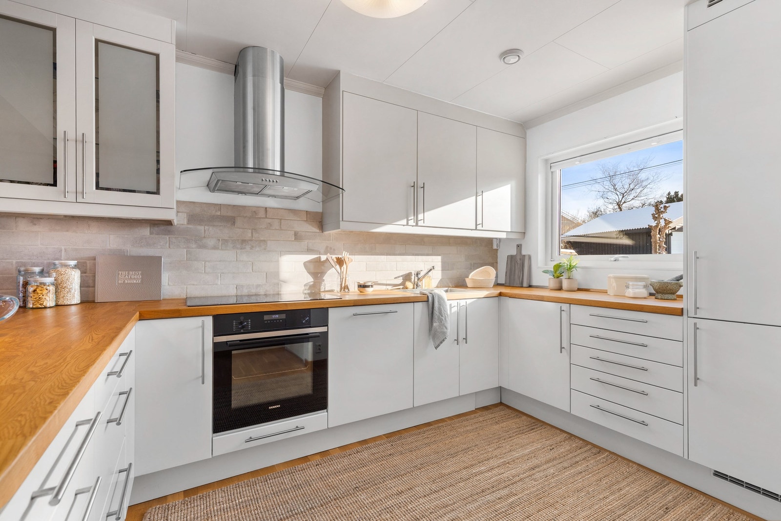 Overskap med vitrinedører. Integrert kjøleskap med fryser, oppvaskmaskin, stekeovn og induksjonstopp. Vegghengt ventilator tilkoblet avtrekk. Galleribilde