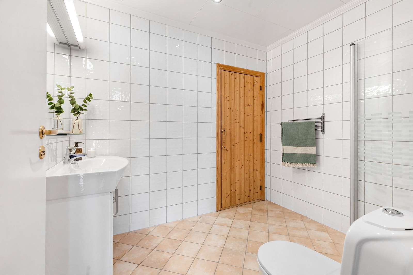 Speil med hylle av glass samt belysning med stikkontakt på vegg over servant. Dusjsone med innfellbare dører av glass. Dusjarmatur tilkoblet hånddusj. Gulvstående toalett. Mekanisk avtrekksventil i himling. Galleribilde