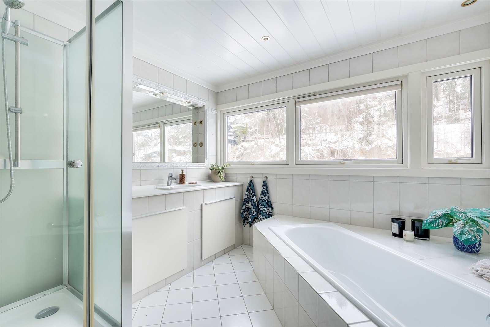 Eldre bad med flis på vegger og gulv, malt panel i taket med dimbare downlights. Badet er innredet med et dusjkabinett. Galleribilde