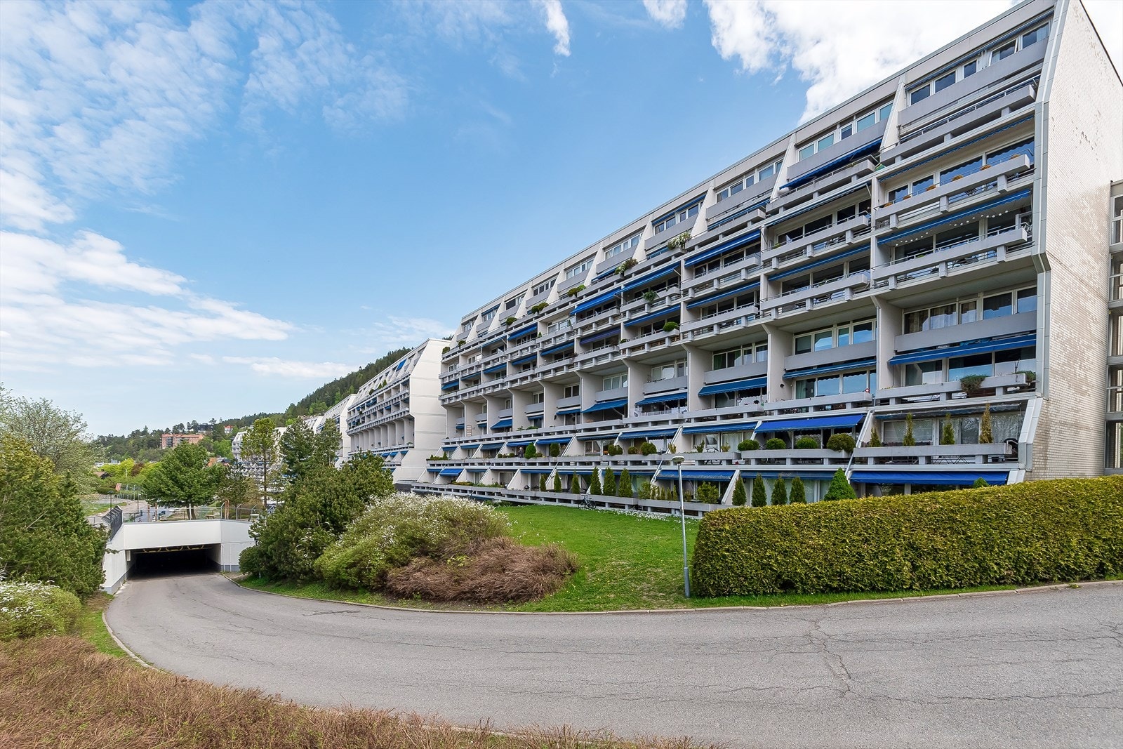 Bilde av boligblokken ved innkjørsel til garasjeanlegget. Tomten er både hyggelig beplantet og grøntområde. Galleribilde