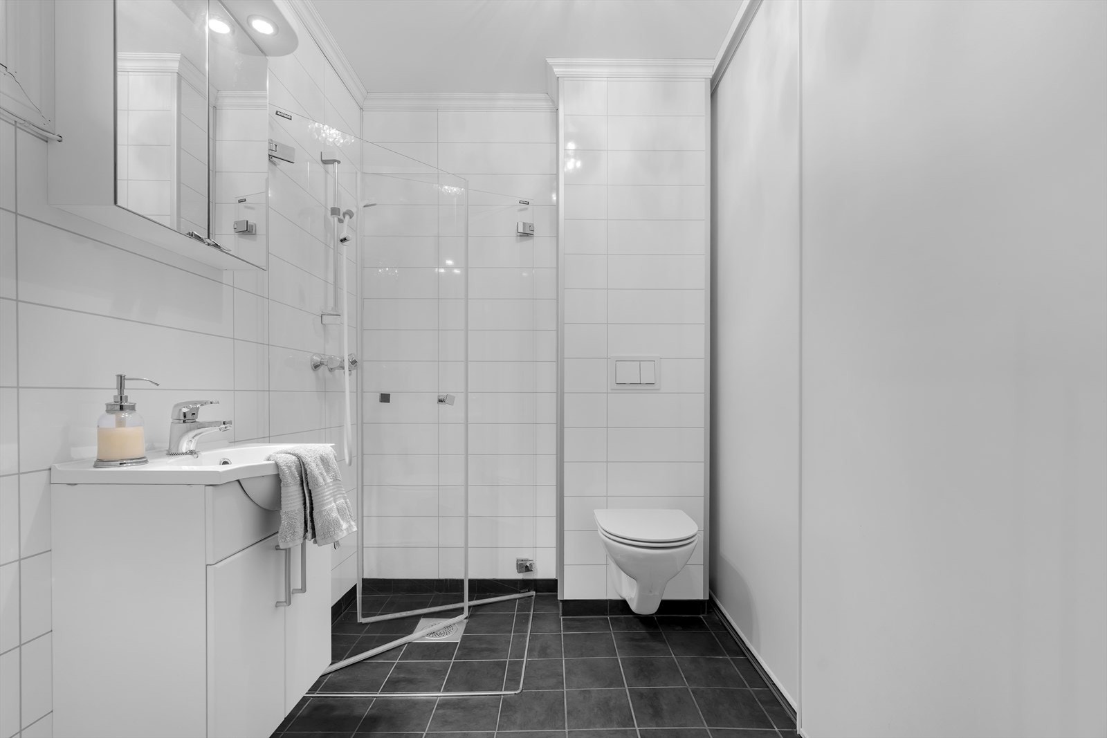 Badet i første etasje er praktisk og funksjonelt utformet. Veggene har pene våtromsplater, mens gulvet er flislagt og utstyrt med gulvvarme for økt komfort. Galleribilde