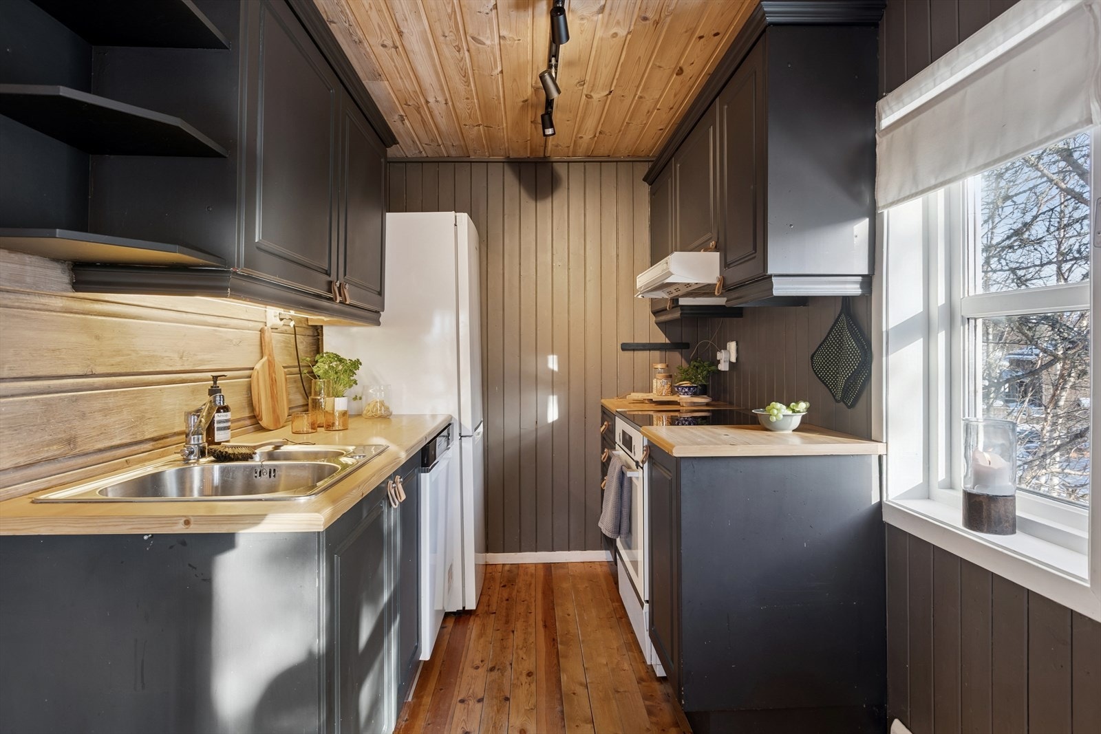 Kjøkkenet har profilerte fronter malt i en moderne, mørk tone som gir et tidløst og elegant uttrykk. Benkeplaten i laminat gir både god slitestyrke og et rent, stilfullt preg. Galleribilde