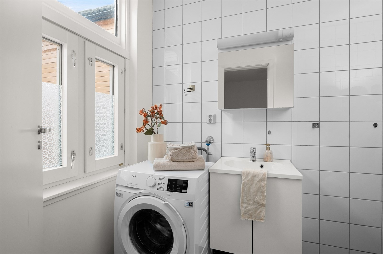 Badet er innredet med dusjvegger av glass og dusjgarnityr på vegg, innredning med servant og opplegg for vaskemaskin. Galleribilde