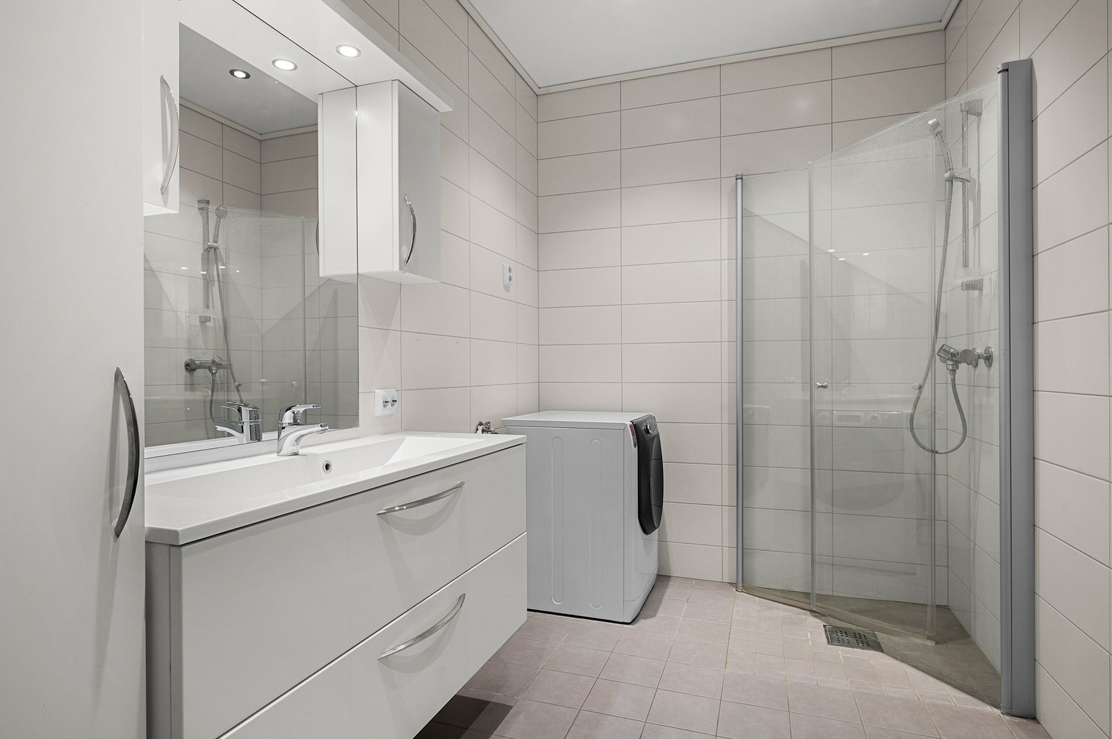 Flislagt bad med stor innredning, hjørnedusj og opplegg til vaskemaskin. Galleribilde