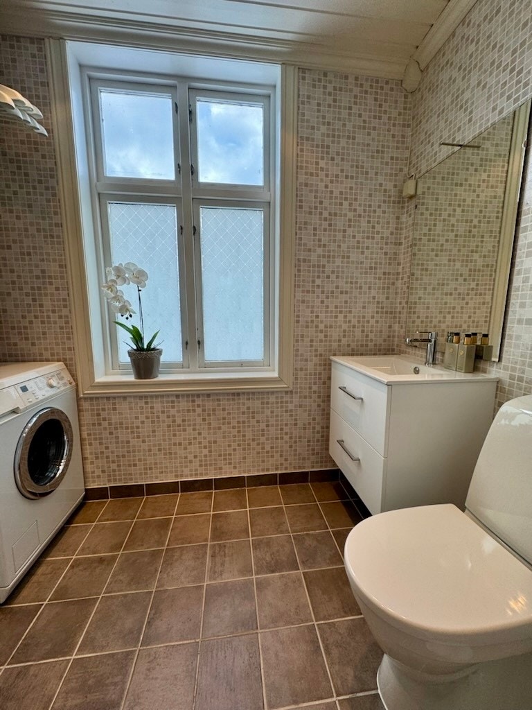 Bad med fliser på gulv, varmekabler i gulv, toalett og baderomsinnredning med servant. Galleribilde