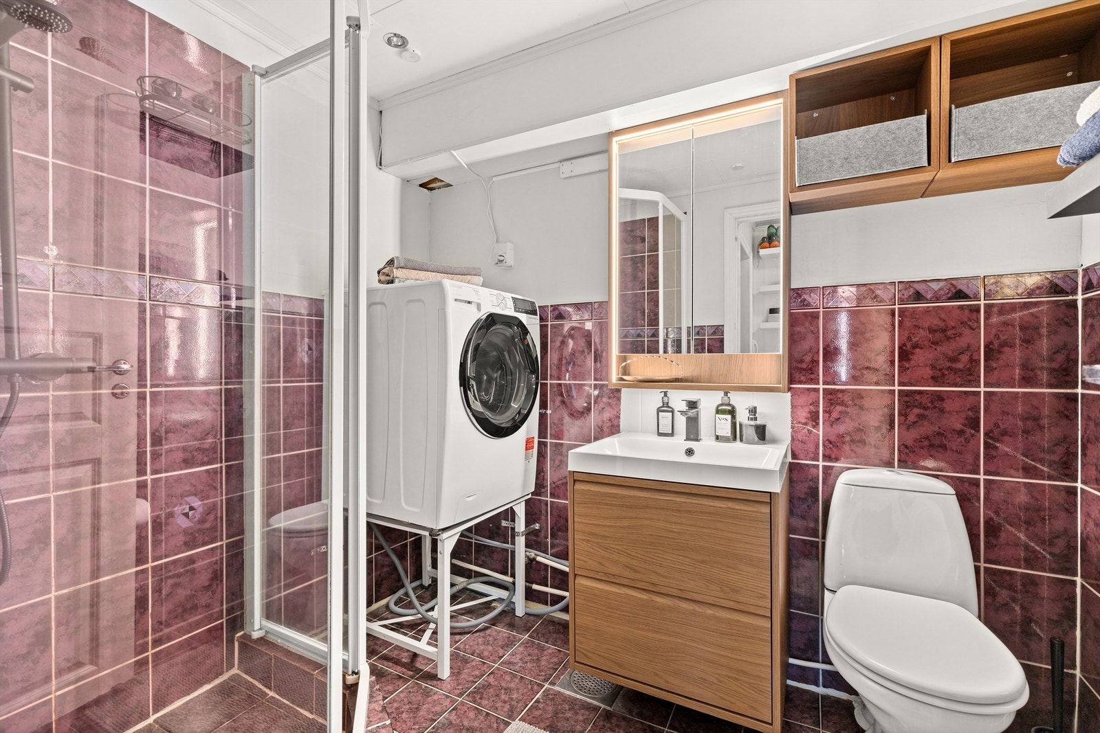 Flislagt bad med dusjkabinett, servantinnredning og praktisk opplegg for vaskemaskin. Galleribilde