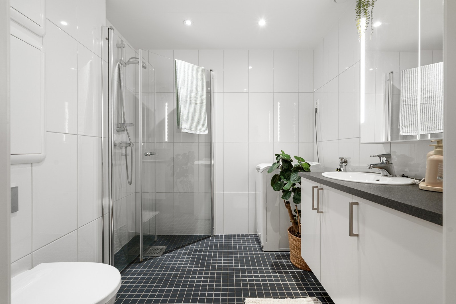 Lekkert, flislagt baderom med lys innredning, toalett, dusjhjørne og opplegg for vaskemaskin. Galleribilde