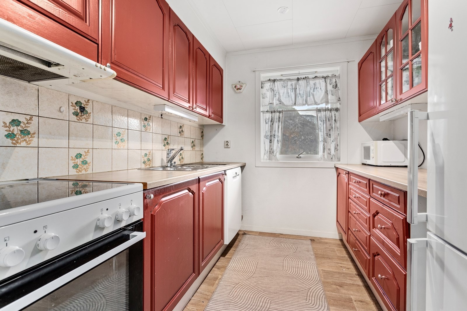 Kjøkken har innreiing med profilerte og måla frontar. Kvitevarer er frittståande og består av komfyr og kombinert frys- og kjøleskåp. Galleribilde