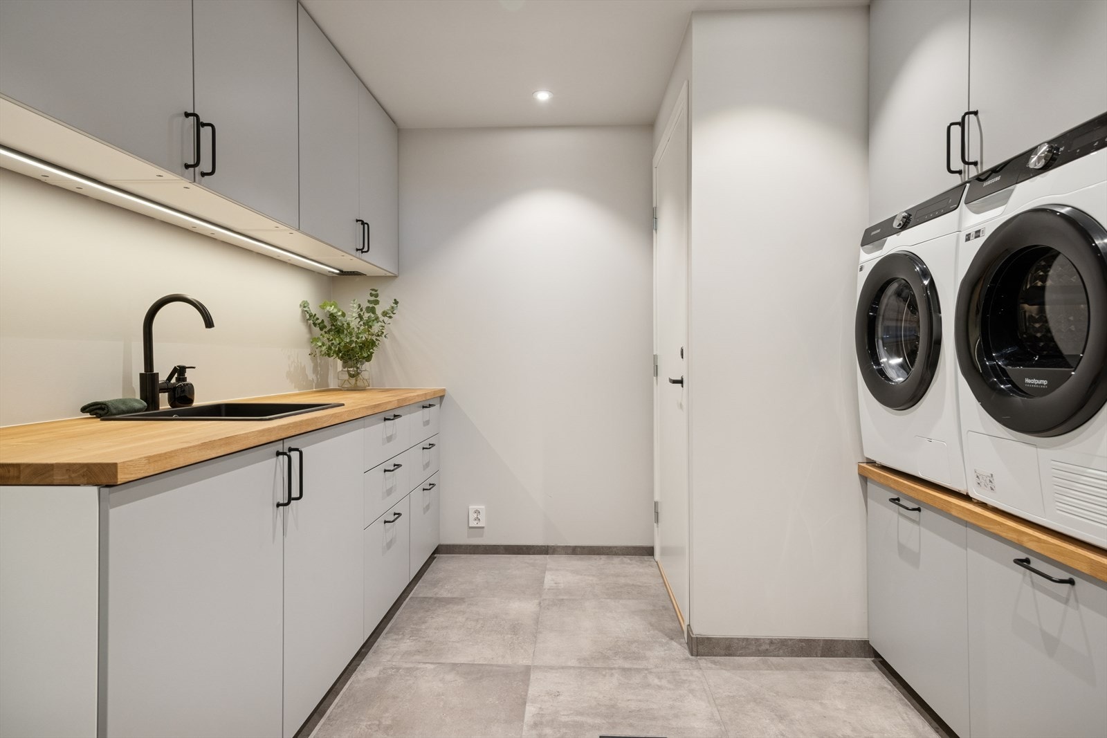 Praktisk vaskerom med rikelig skap- og benkeplass. Opplegg for både vaskemaskin og tørketrommel gir en funksjonell og ryddig arbeidsplass i hverdagen. Galleribilde