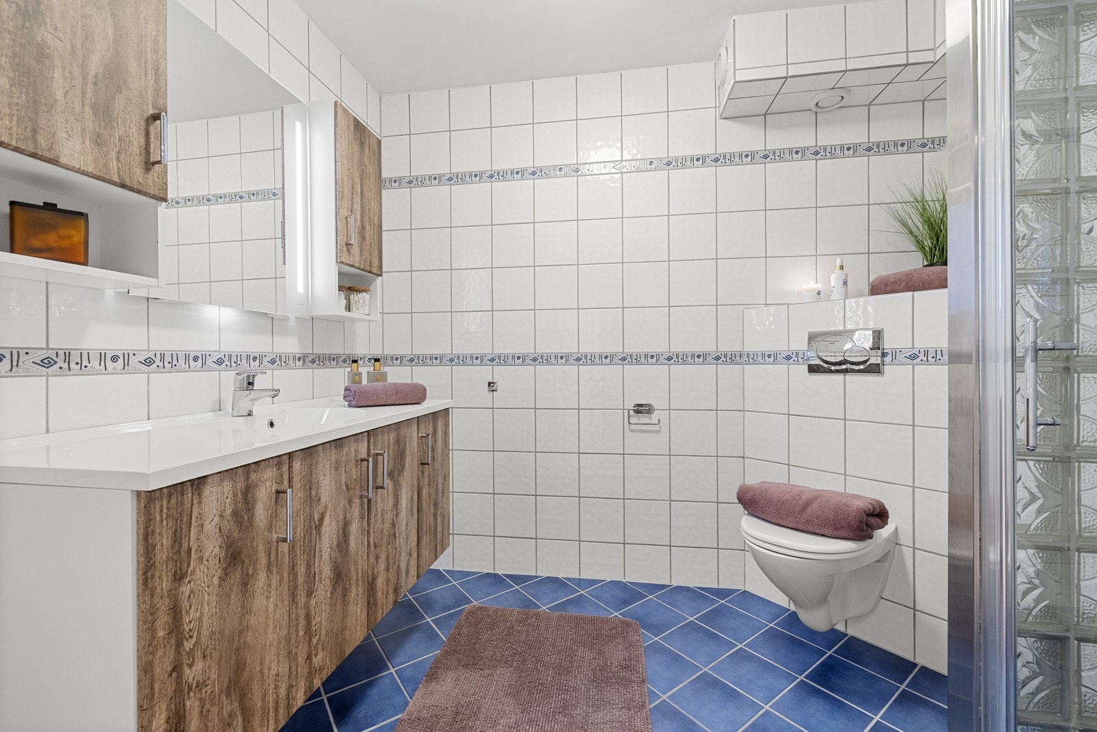 Romslig og delikat baderom med speil og belysning over servant, gode oppbevaringsløsninger og behagelige varmekabler i gulv. Galleribilde