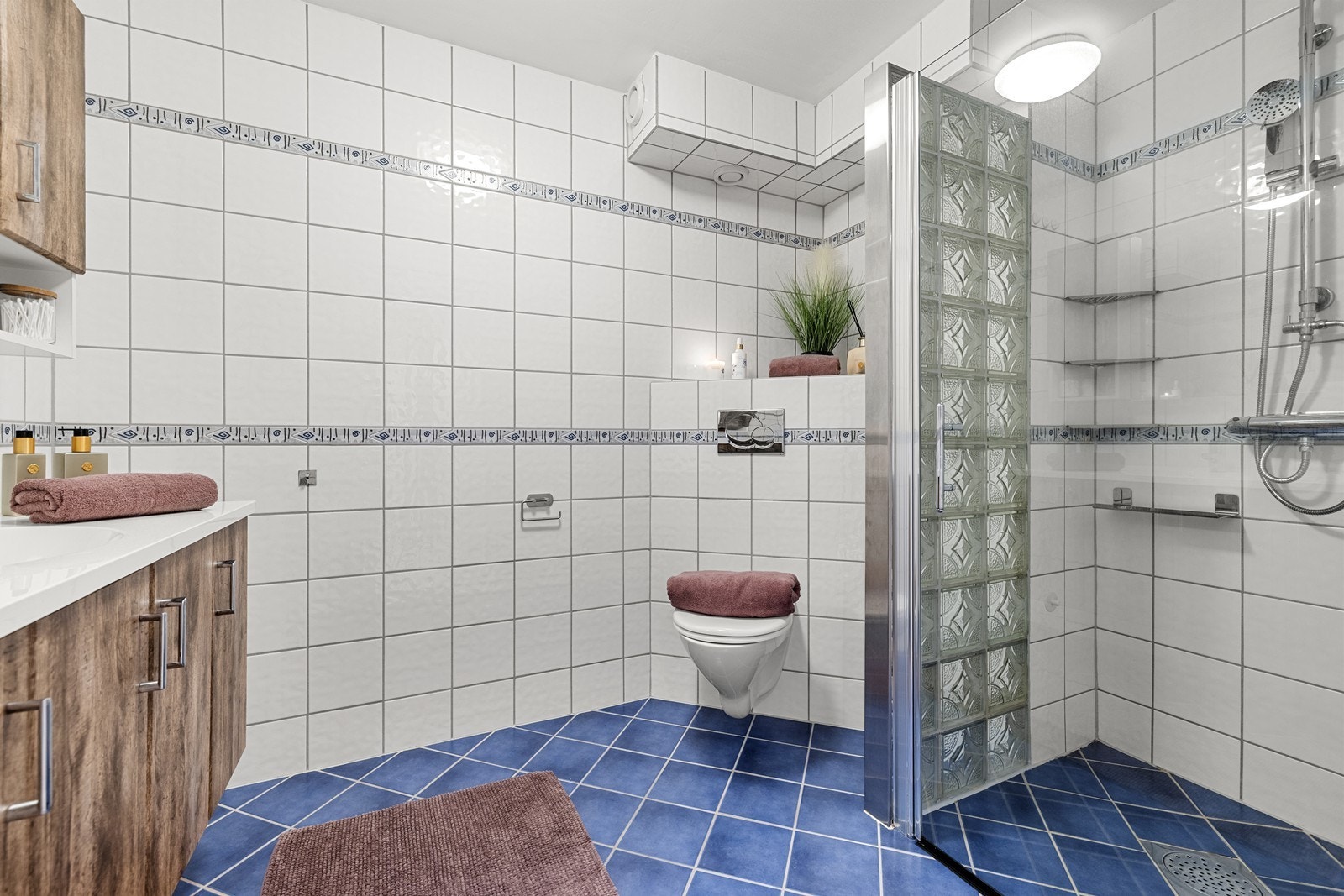 Flislagte gulv og vegger, vegghengt toalett, servant med underskap og dusjnisje med glassdør. Galleribilde