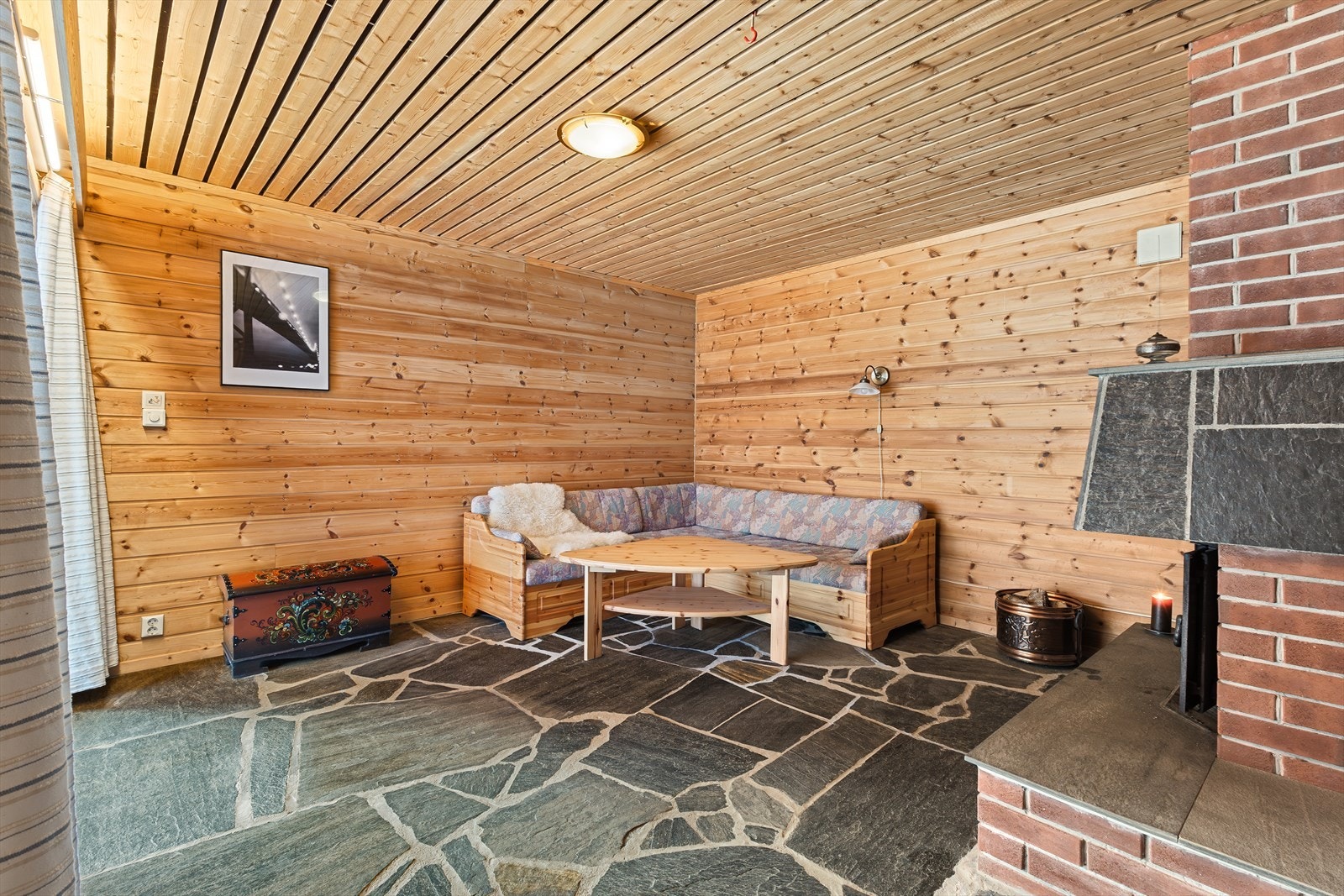 Skyvedører slipper inn rikelig med dagslys, og rommet har en koselig peisovn. Herfra er det utgang til en pen uteplass i front av boligen Galleribilde