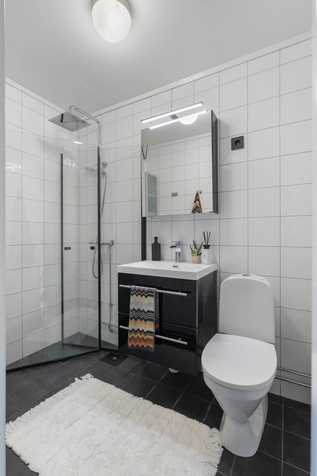 Det er fint bad med fliser på gulv og vegger. Badet er inneholdende toalett, innredning med servant og dusj/vegger. Galleribilde