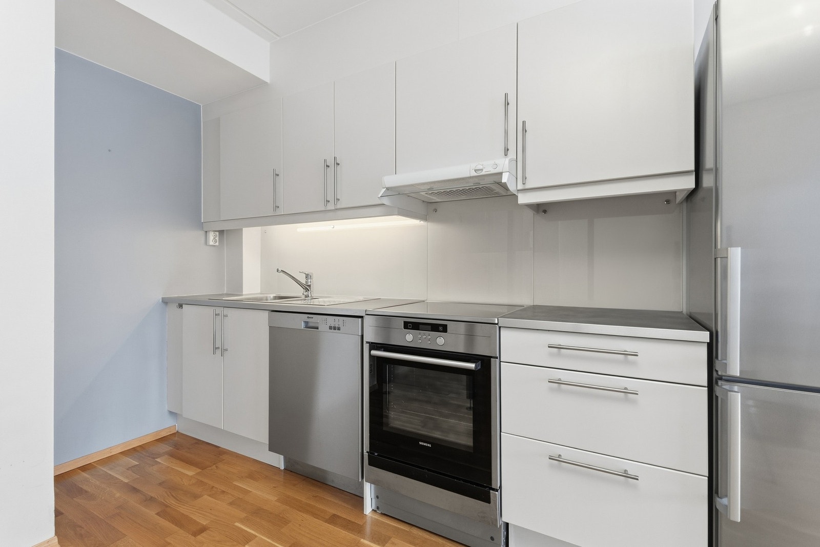 Innredningen har glatte fronter, laminert benkeplate og glassplate mellom over- og underskap. Her får du god skap- og benkeplass samt plass til hvitevarer. Galleribilde