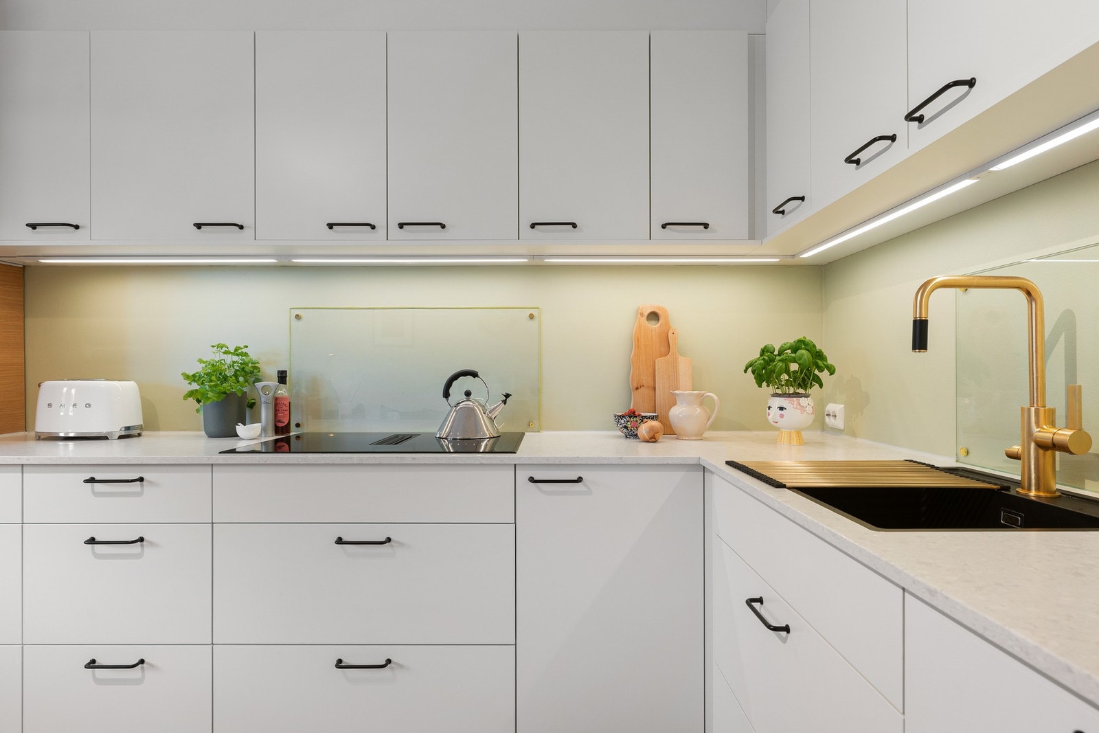 Delikat arbeidsområde med god benkeplass, planlimt kum og armatur i børstet utførelse. Integrert koketopp og overskap med belysning gir både funksjonelt arbeidslys og et moderne uttrykk. Galleribilde