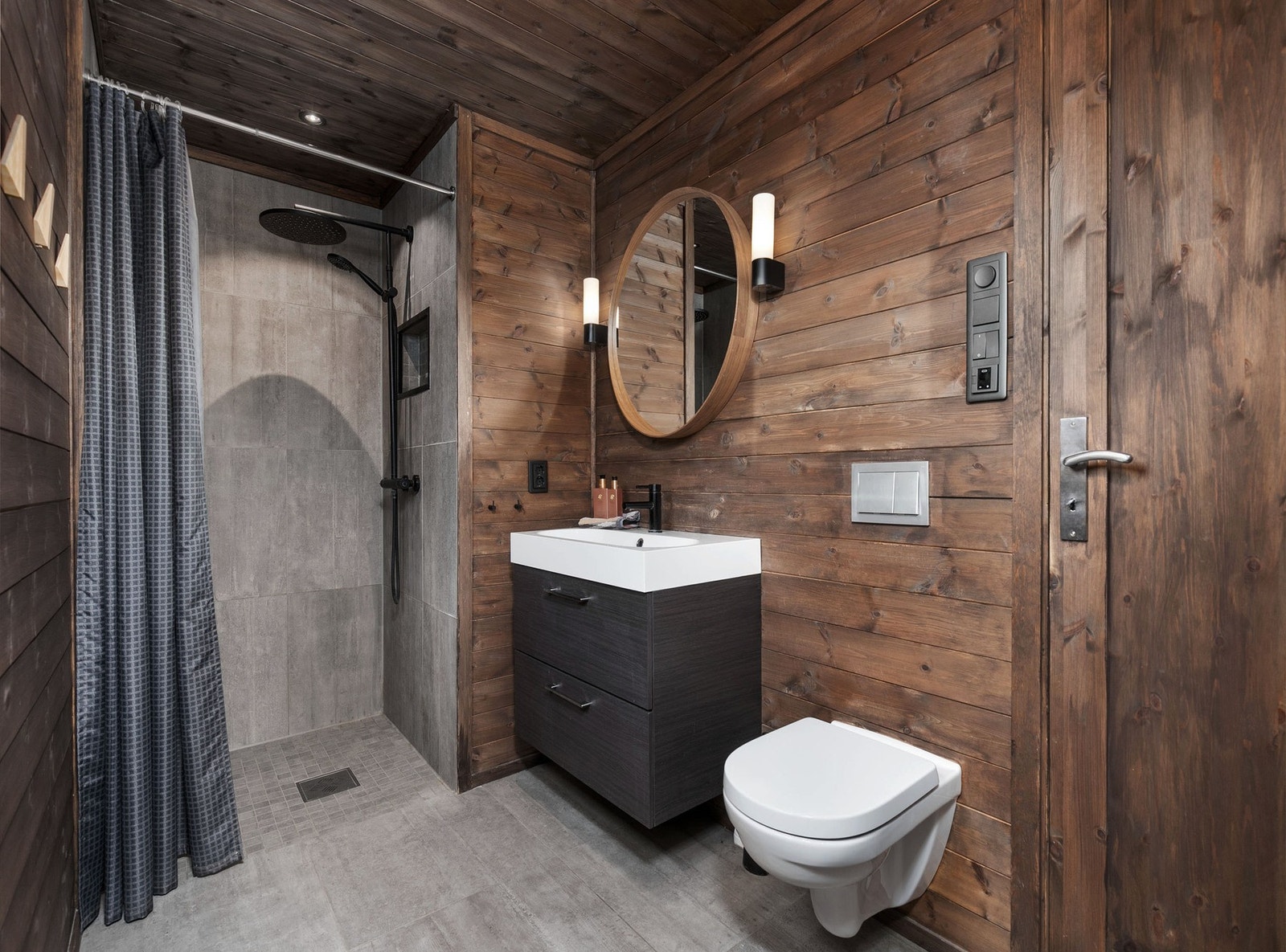 Pent bad- og kombinert vaskerom i 1.etasje med fliser på gulv med gulvvarme og beiset panel kombinert med fliser i dusjsonen. Galleribilde