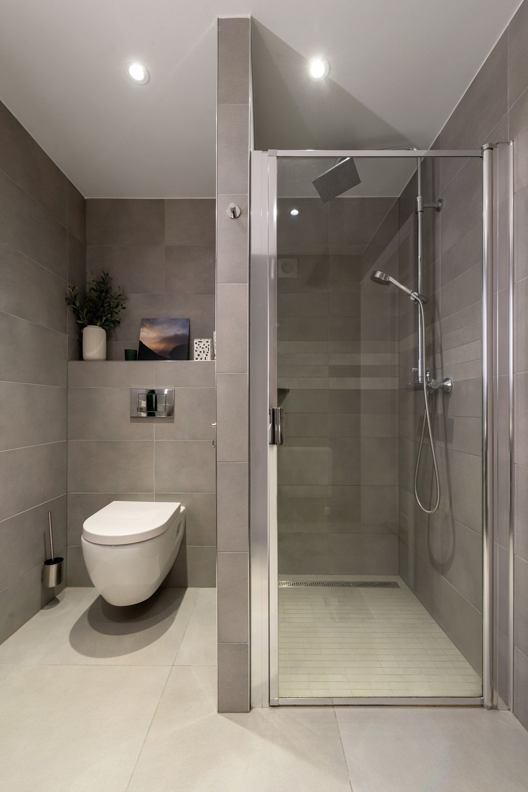 Rommet er utstyrt med en dusjnisje med glassdør og et vegghengt toalett med innebygget sisterne. Galleribilde