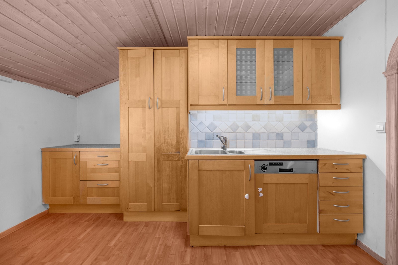 Fliser på vegg over benk gir et robust arbeidsområde, med oppvaskmaskin integrert under benkeplaten. Galleribilde