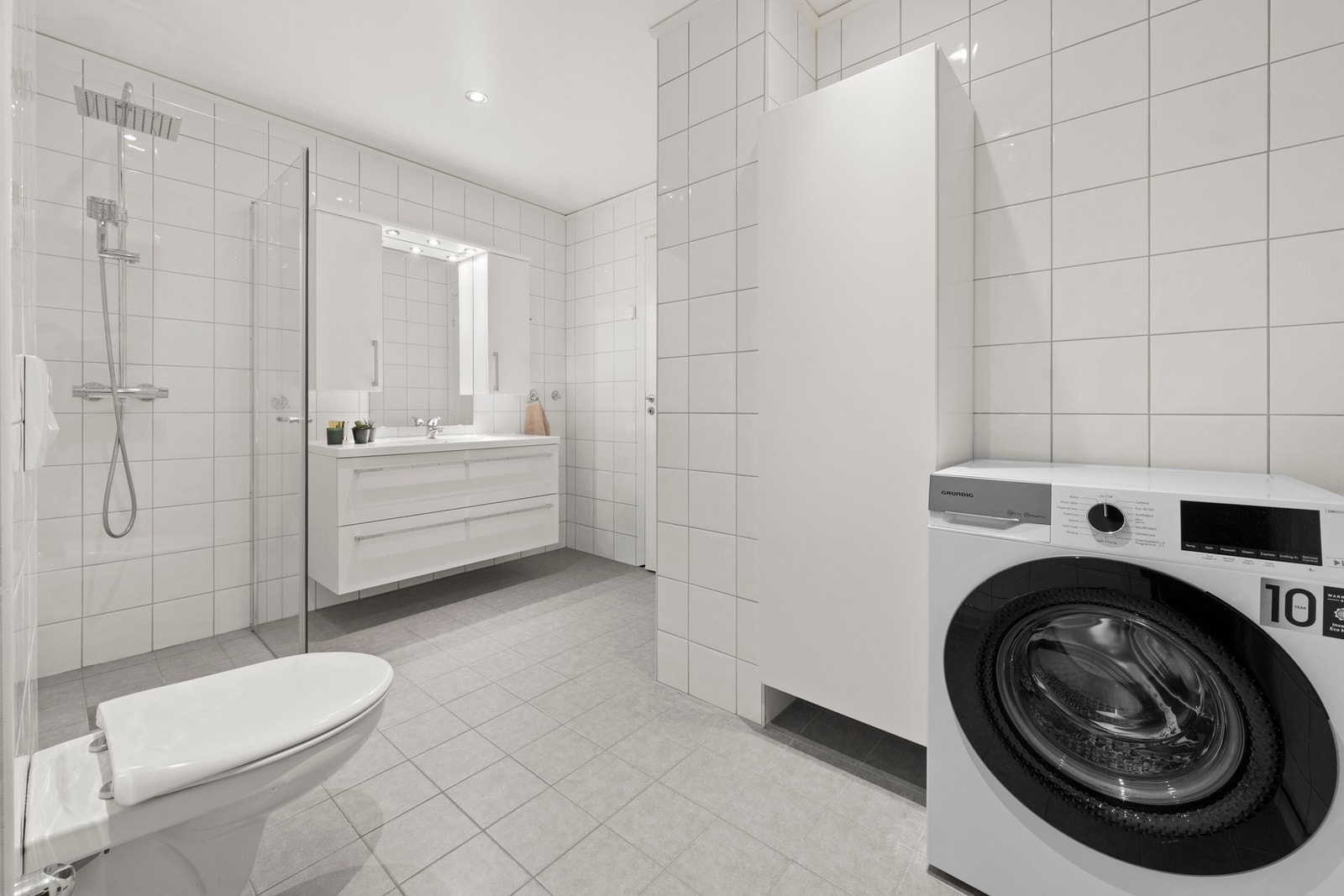 Badet er praktisk innredet med dusjhjørne med glassdører, vegghengt toalett og servant med speil. Det er opplegg for vaskemaskin og god plass til tørketrommel Galleribilde