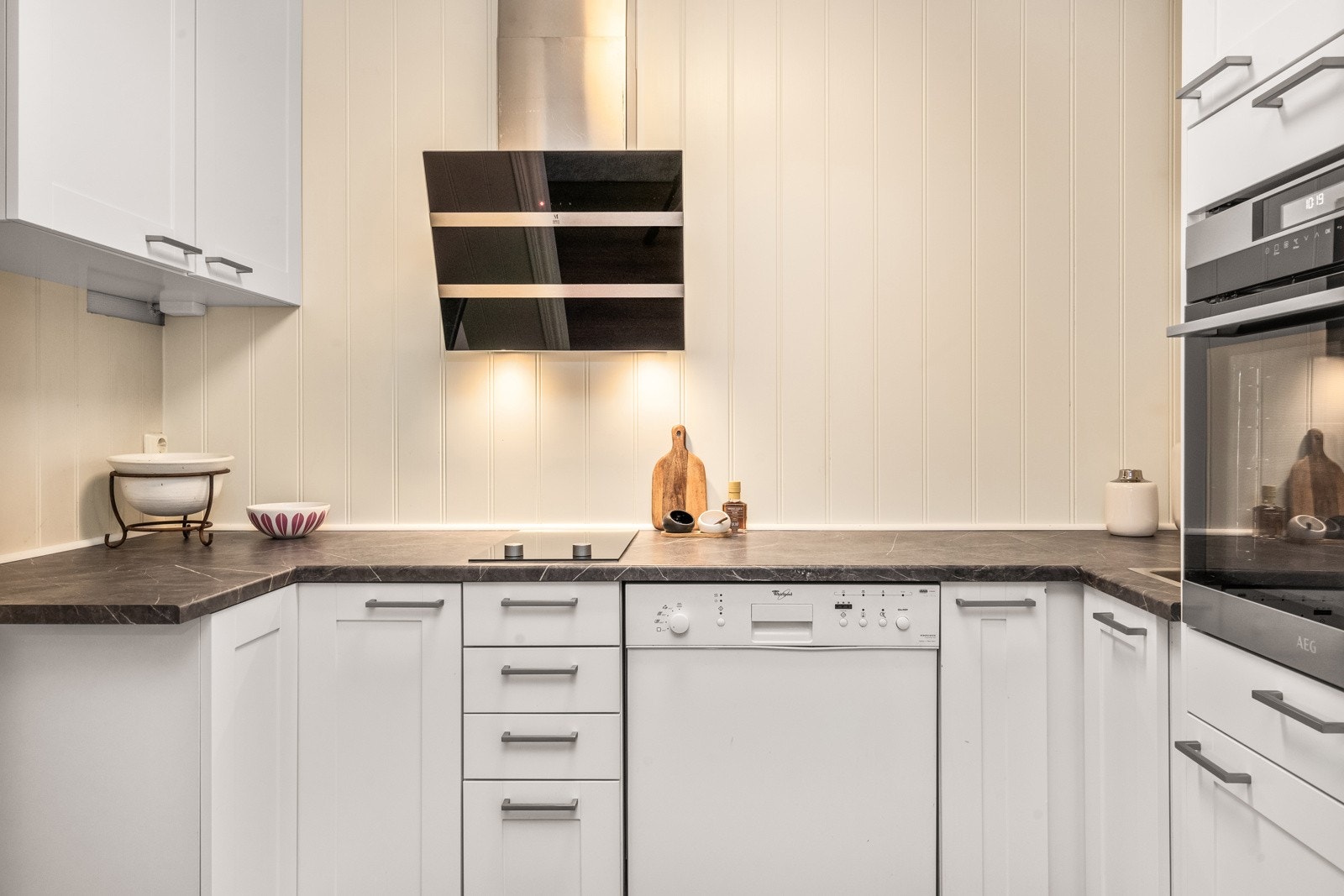 Innredning av hvite, profilerte fronter, laminat benkeplate med planlimt kum i rustfritt stål. Galleribilde