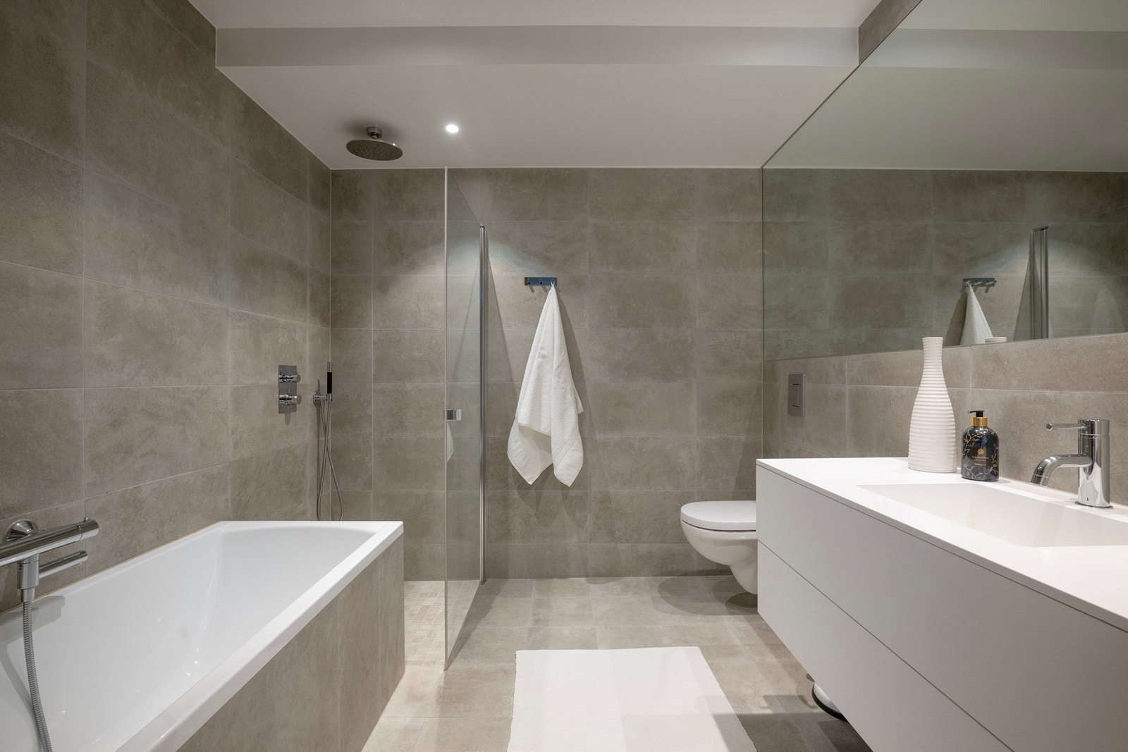 Hovedbaderommet er flislagt med store fliser i en tidløs farge med varme i gulv. Galleribilde