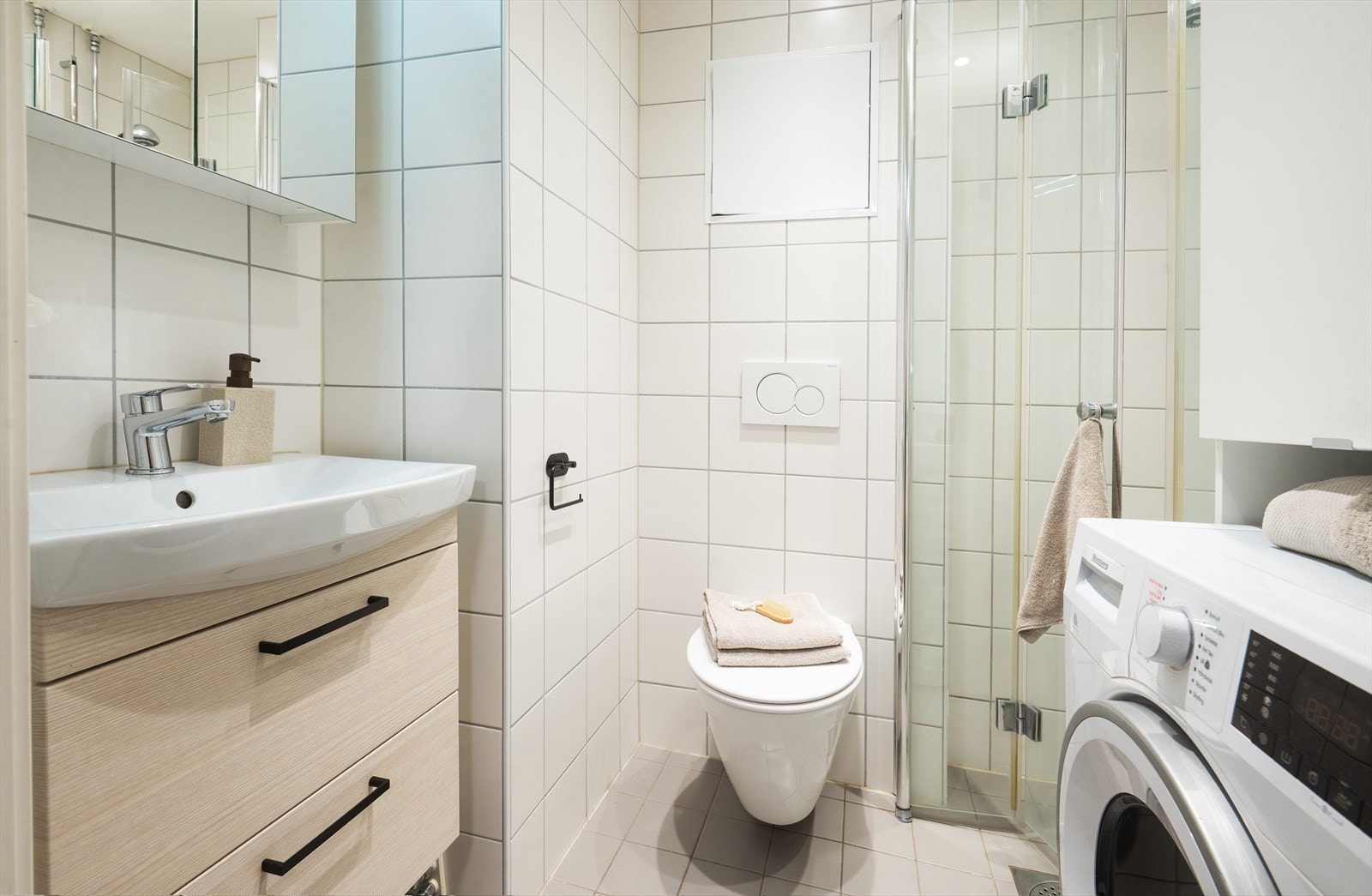 Rommet er utstyrt med vegghengt toalett, dusjhjørne med glassdører og opplegg for vaskemaskin. Galleribilde