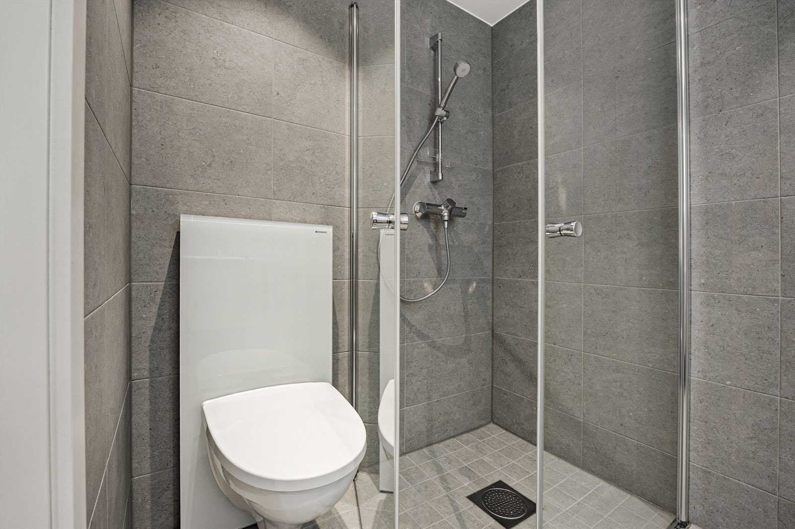 Detaljer fra badet som viser dusjløsningen og det vegghengte toalettet. Galleribilde