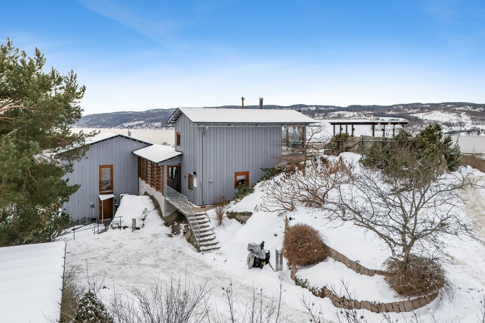 Trapper og terrasseringer gir diverse rekreasjonssoner med drivhus, lekehus, sandkasse, plaskedam, et utall av busker og stauder, plen, beplantede krukker og kasser som pryder eiendommen Galleribilde