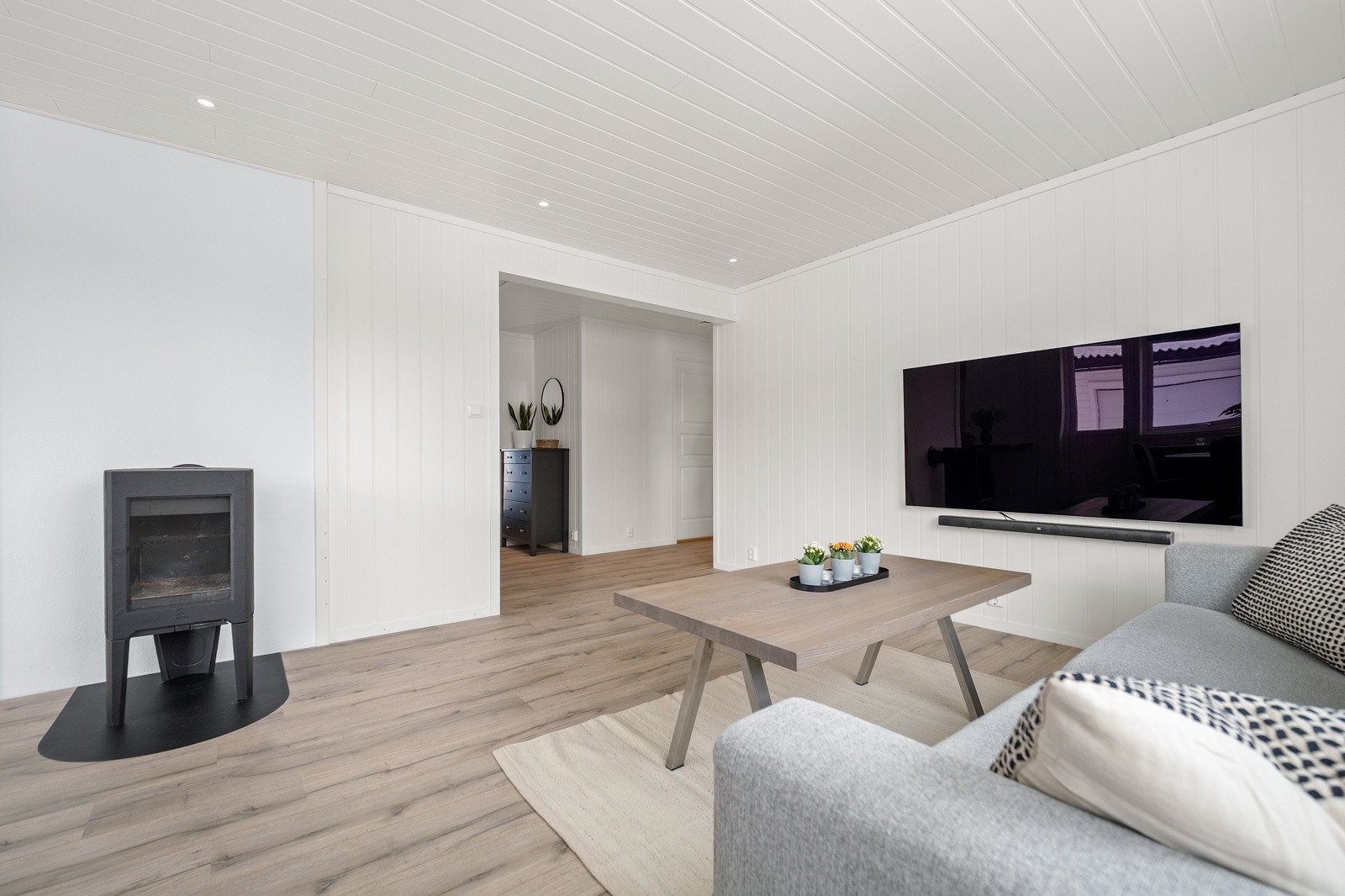 Stuen er et lyst og åpent rom med en sentralt plassert vedovn for varme og hygge Galleribilde