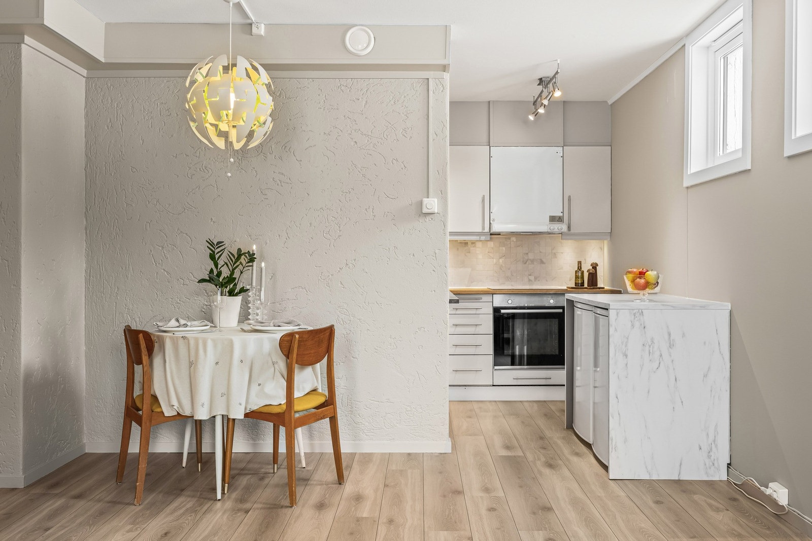 Praktisk kjøkkenkrok med innredning i funksjonell L-form, suppleres av en benkeløsning i laminat med marmormønster Galleribilde