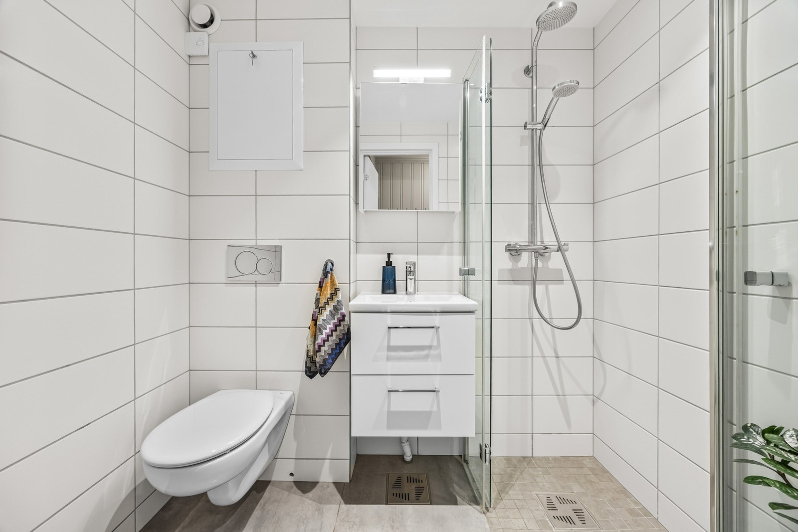 Badet ble pusset opp i 2019, smakfullt innredet med hvite veggfliser og store, lysegrå gulvfliser Galleribilde