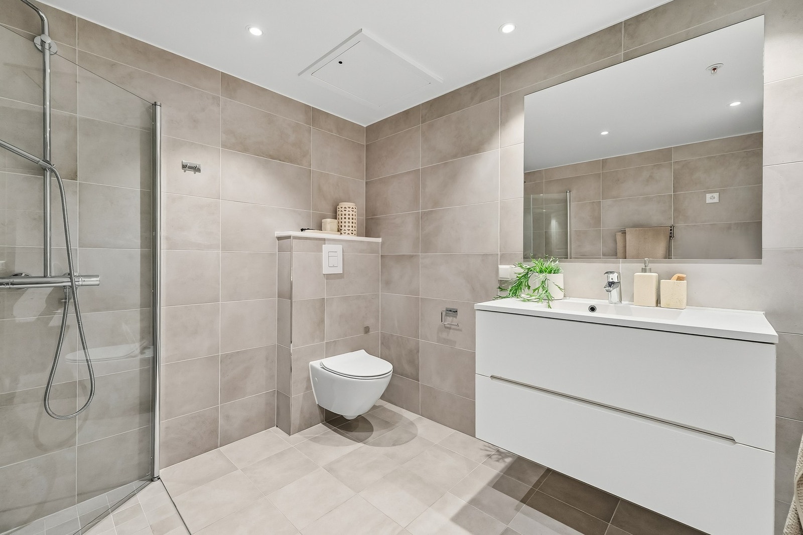 Romslig og delikat bad med flislagte overflater, moderne innredning og vegghengt toalett. Stilrent uttrykk kombinert med god funksjonalitet. Galleribilde