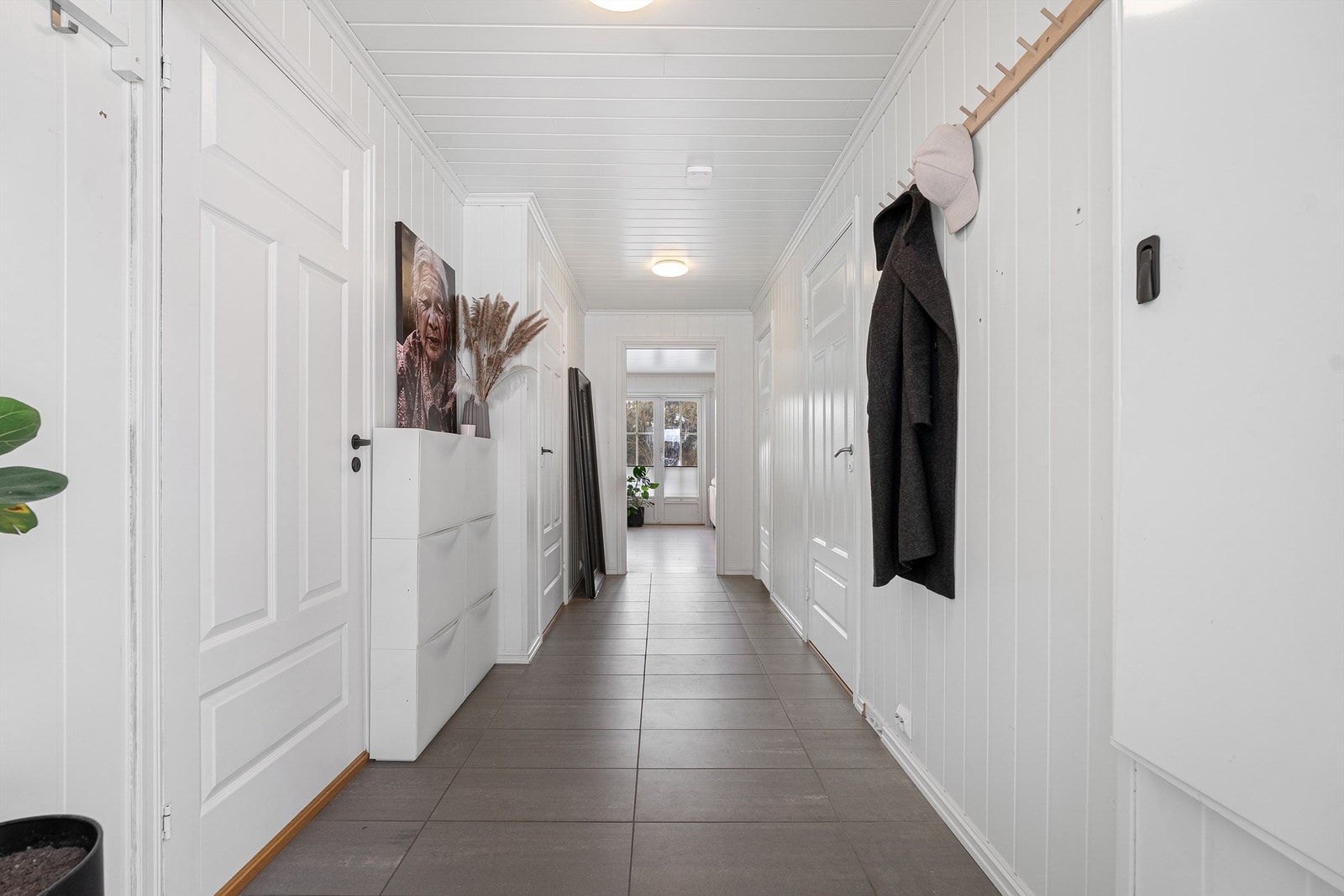 Stor og langstrakt gang m gulvvarme, med direkte tilgang til boligens bad og to soverom og bod utenfor inngangen Galleribilde