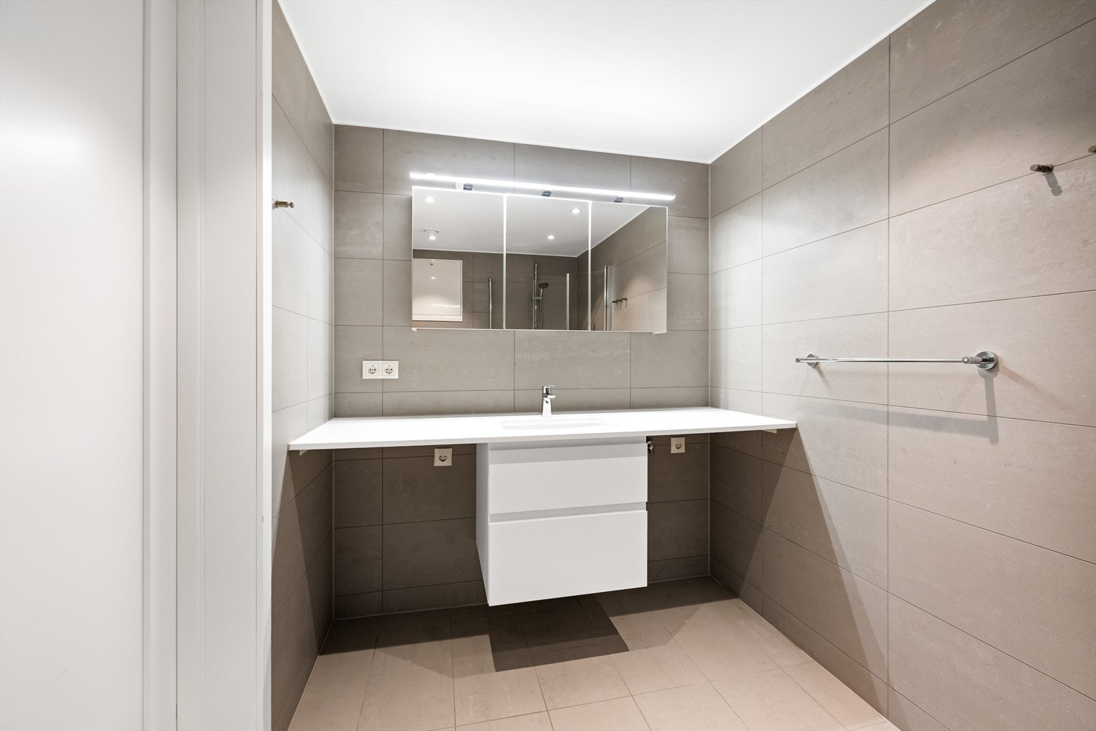 Badet er utstyrt med dusj med innfellbare glassvegger, vegghengt toalett, servantinnredning med underskap og speilskap med belysning, samt opplegg for vaskemaskin og tørketrommel Galleribilde