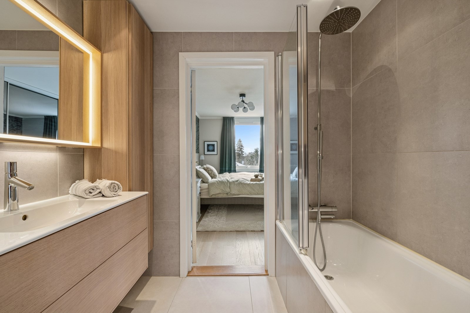 Badet er innredet med servantskap med ett-greps blandebatteri, veggskap, høyskap, speil med lys, innmurt badekar, glassvegg på badekarskant, blandebatteri og dusjgarnityr. Galleribilde