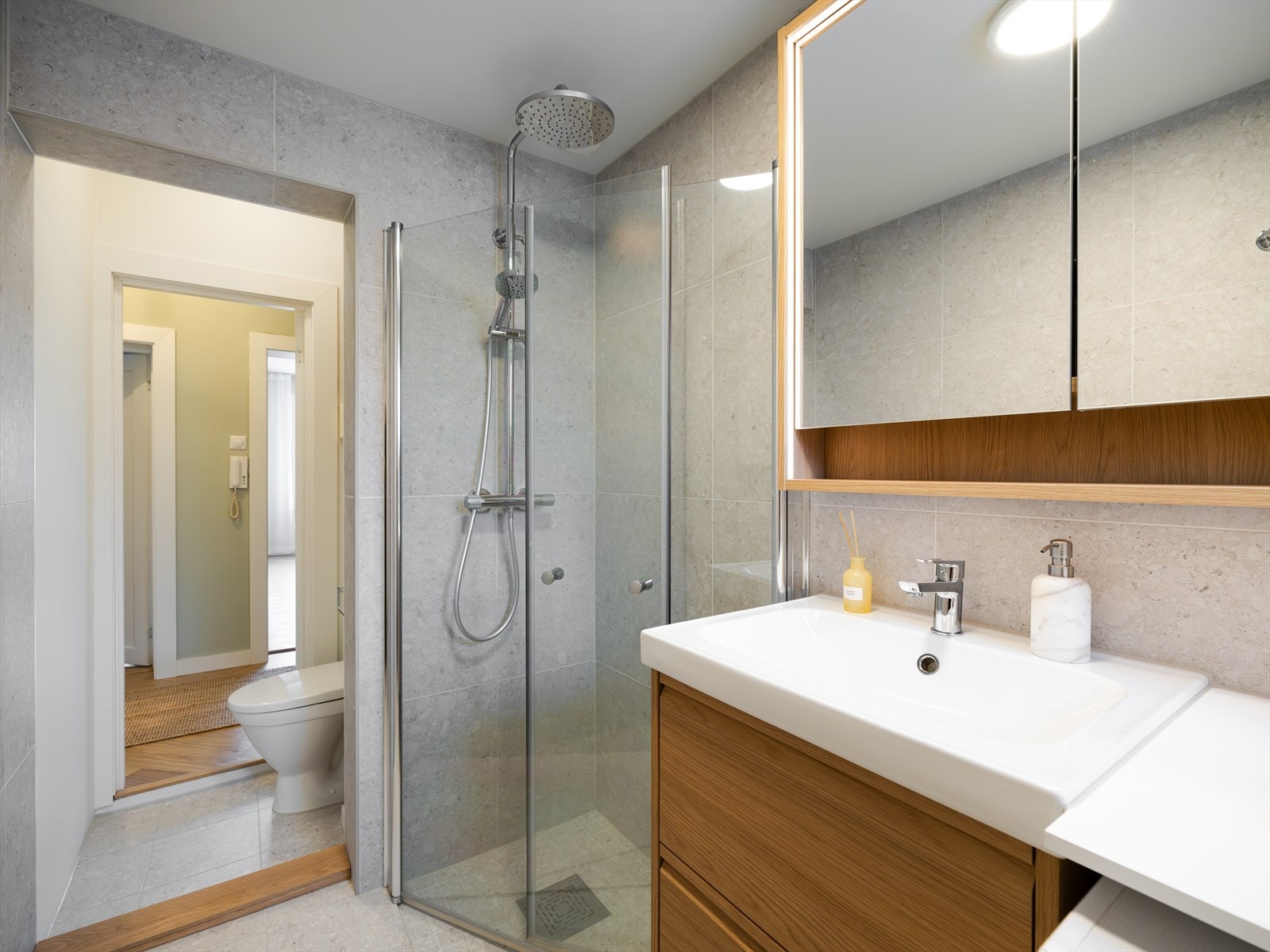 Veggene i badedelen er kledd med stilrene fliser i stort 60 × 60-format som gir et eksklusivt og helhetlig uttrykk, mens toalettdelen har slette, malte flater som tilfører rommet en lett og elegant kontrast Galleribilde