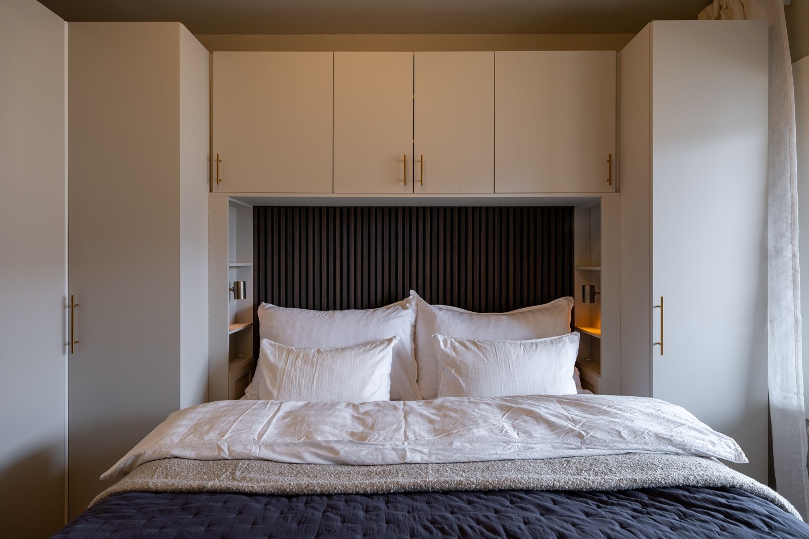 Rommet har god plass til dobbeltseng og er innredet med en plassbygget garderobeløsning som rammer inn sengen på en stilfull måte Galleribilde