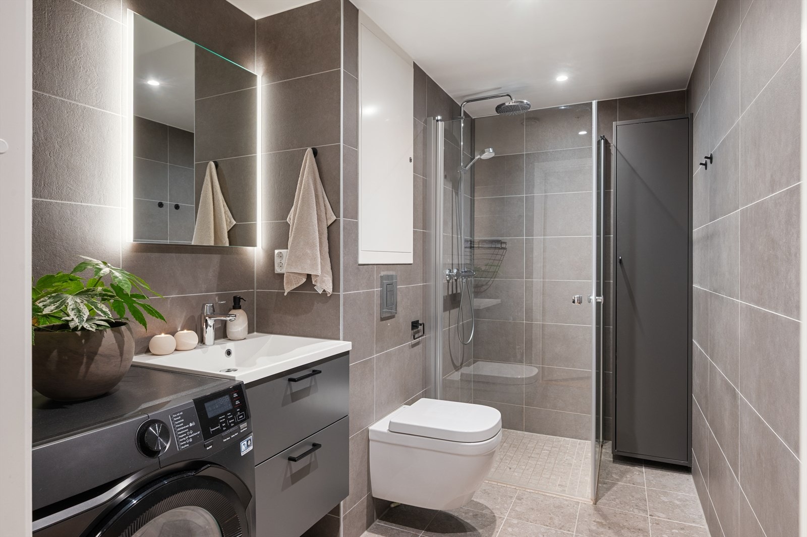 Pent bad med vegghengt toalett, servant med innredning og speil med lys. Galleribilde