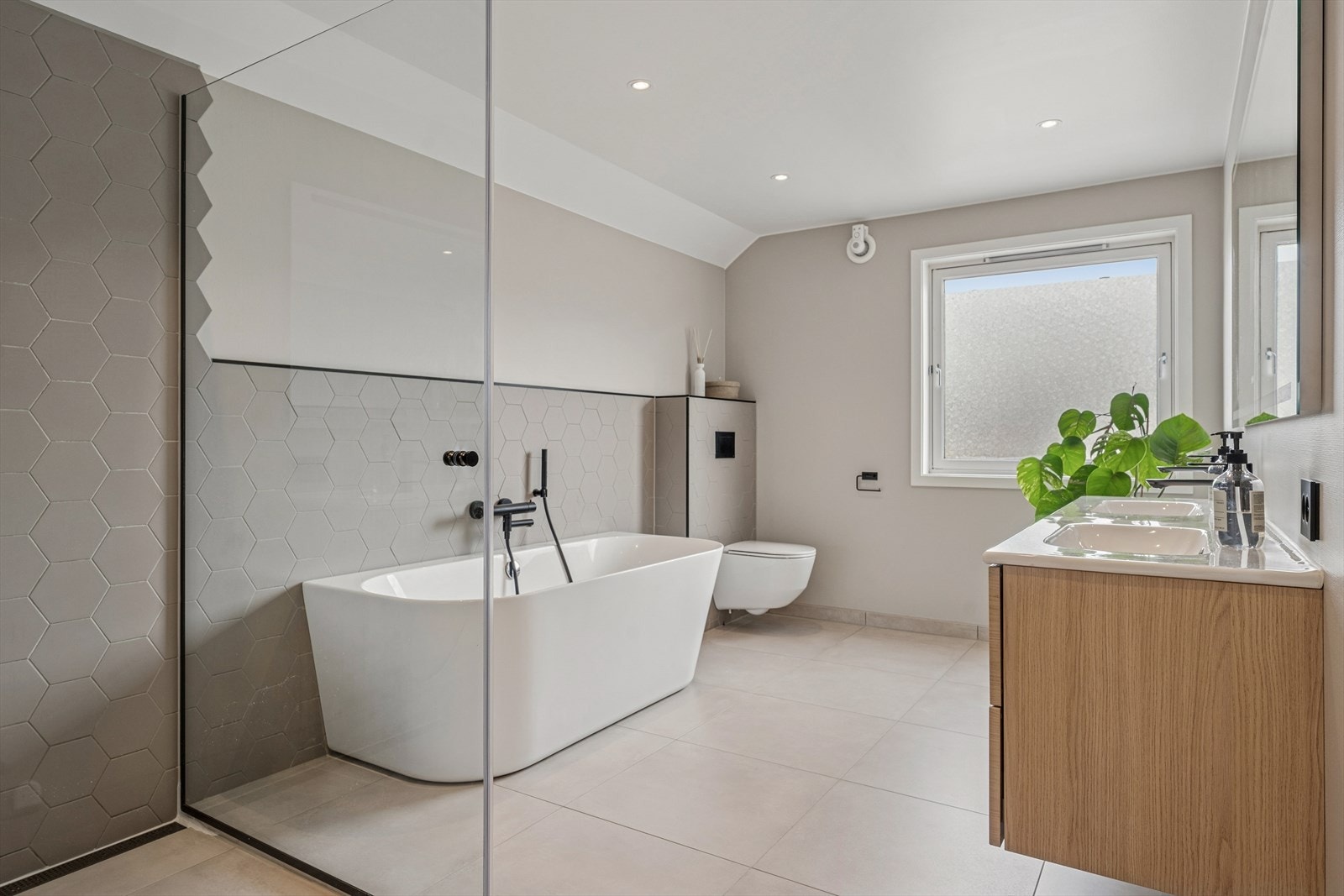 Badet ble renovert i 2022 og er lekkert innredet med store grå fliser på gulvet og en kombinasjon av grå hexagonfliser og malte flater på vegg. I gulvet har man også varmekabler for ekstra komfort. Galleribilde