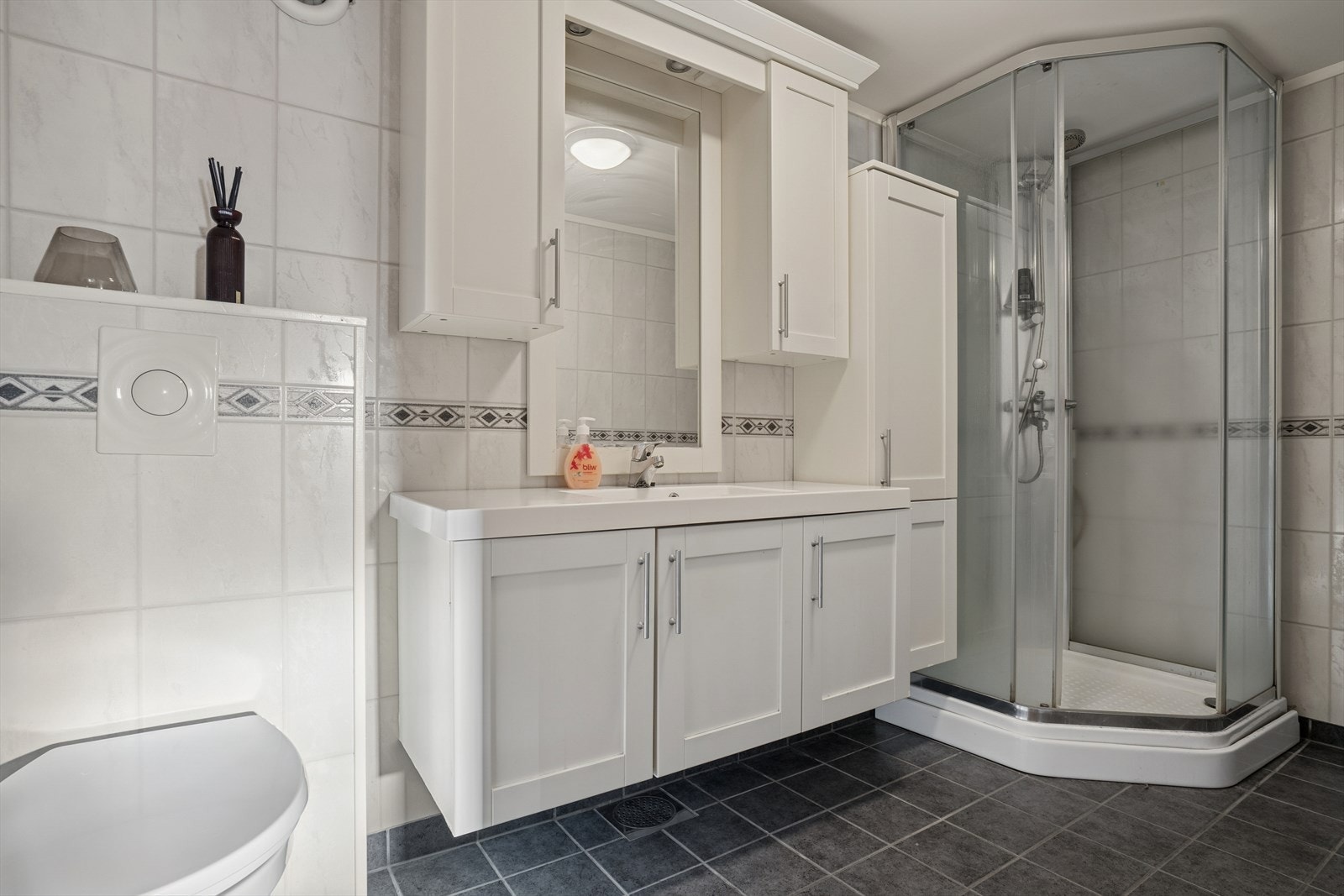 Badet i underetasjen er lyst og innbydende, med flislagt gulv m/varmekabler og vegger med baderomsplater i flisimitasjon - Her finner du vegghengt toalett, dusjkabinett og baderomsinnredning Galleribilde