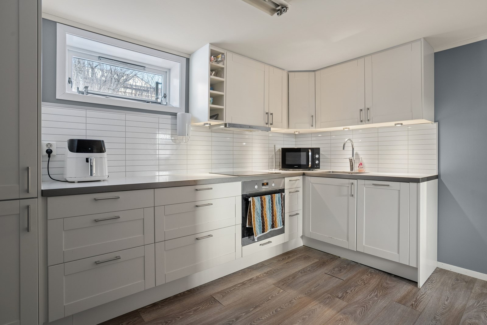 Også kjøkkenet i underetasjen er oppgradert i nyere tid - Det er profilerte grå fronter, benkeplate i laminat som gir en praktisk arbeidsflate og plater i flisimitasjon på vegg over benk Galleribilde