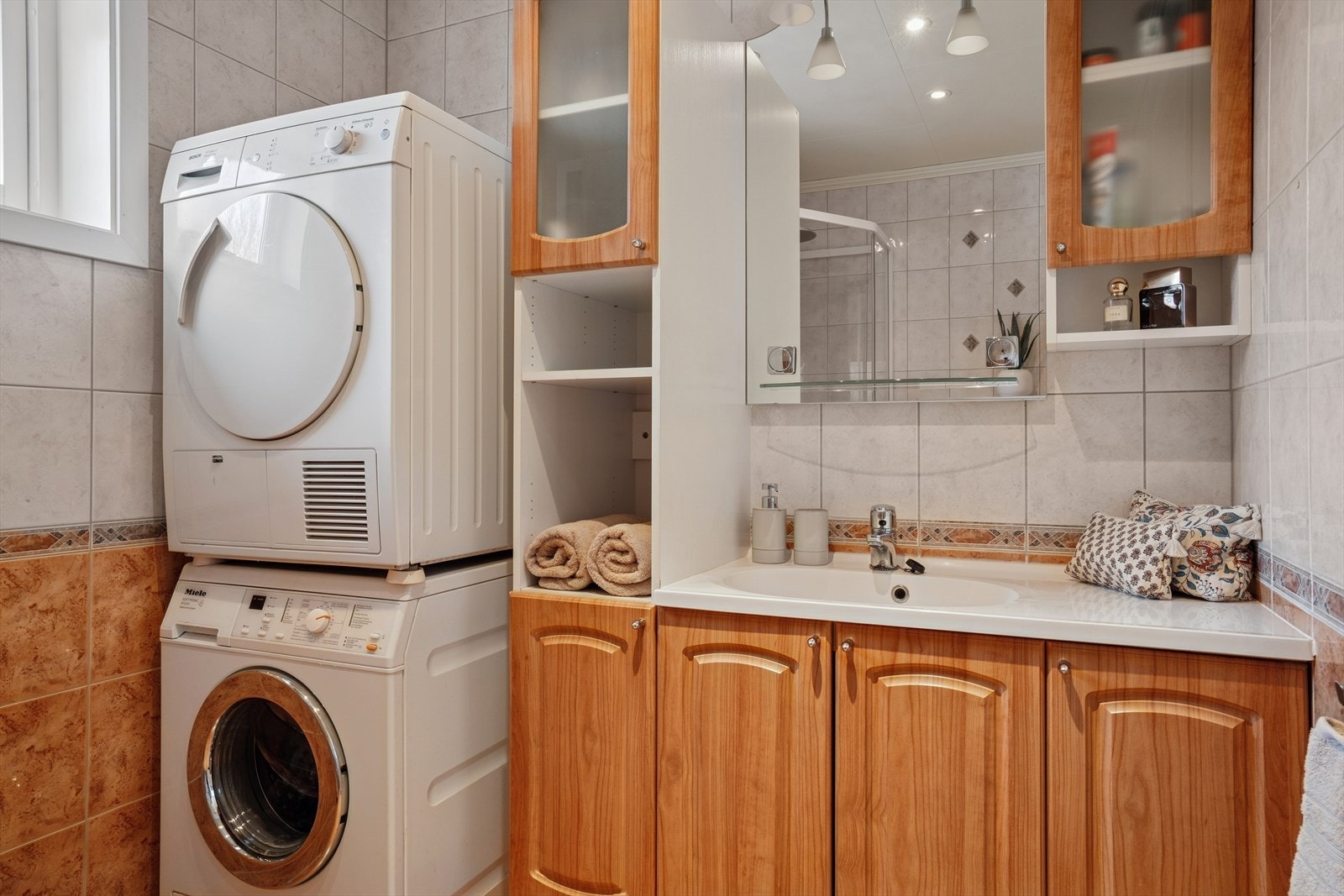 Her finner du veggmontert toalett, dusjkabinett, baderomsinnredning og opplegg for vaskemaskin/tørketrommel - Innredningen består av servant med flere romslige skap rundt og speil på vegg over Galleribilde