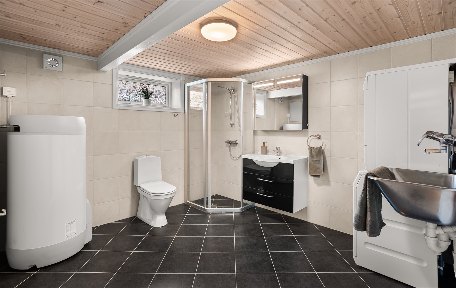 Praktisk kombinert bad og vaskerom med dusjnisje, utslagsvask og opplegg for vaskemaskin. Galleribilde